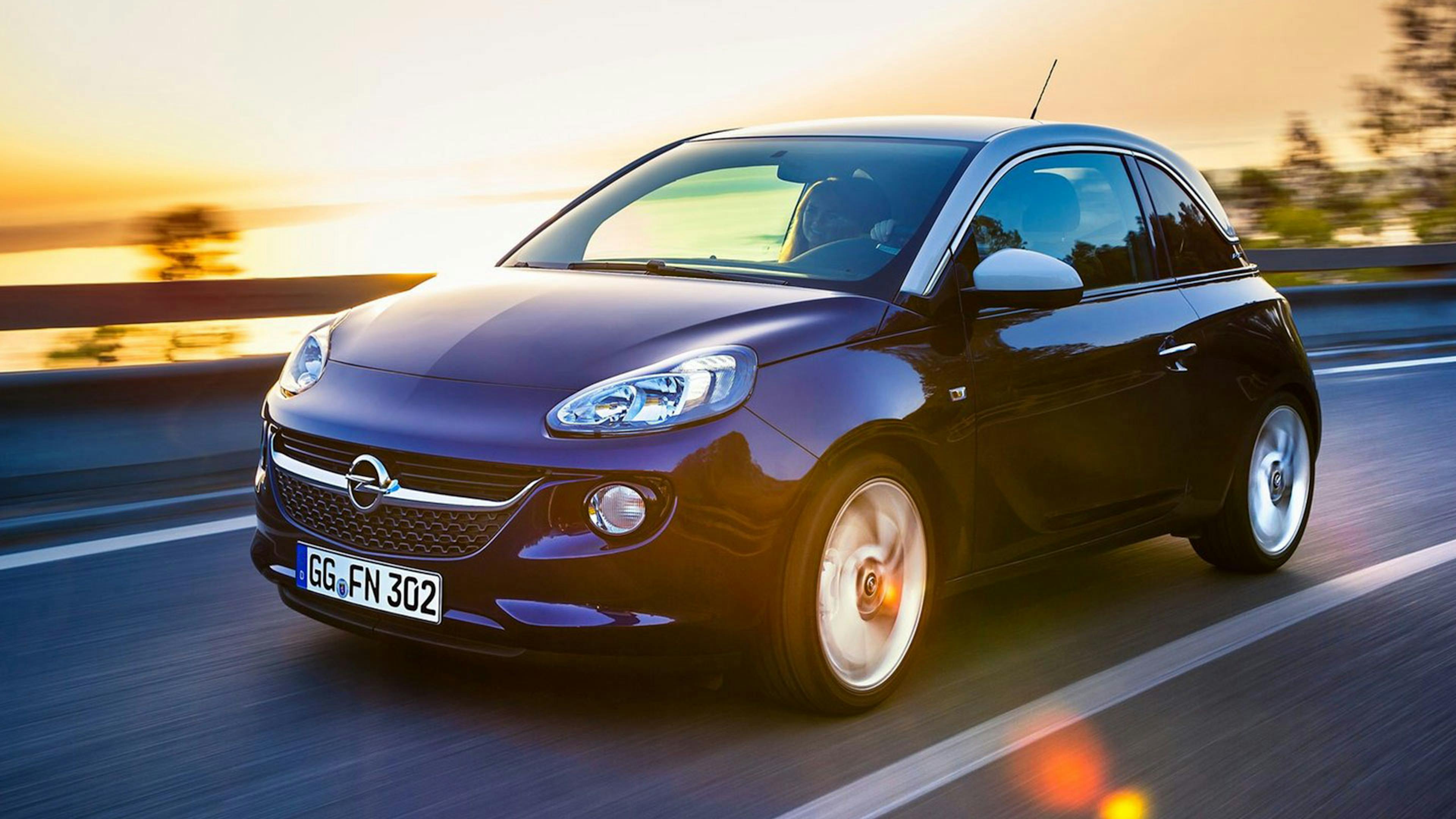 Ein dunkelblauer Opel Adam Kleinstwagen fährt eine Landstraße entlang.