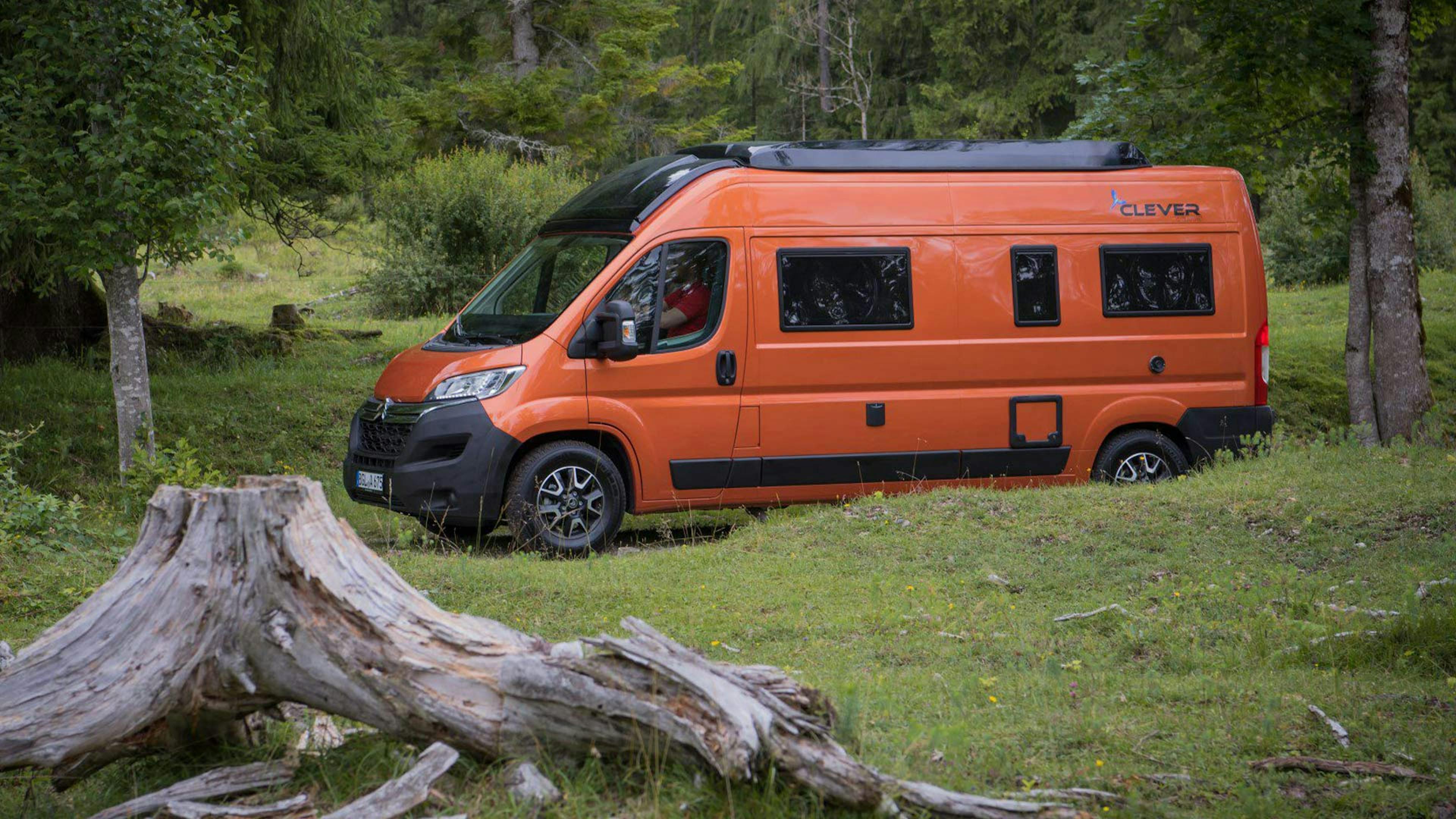 Ein orangefarbener Clever Vans Vario Kids 600 Campingbus fährt durch einen Wald