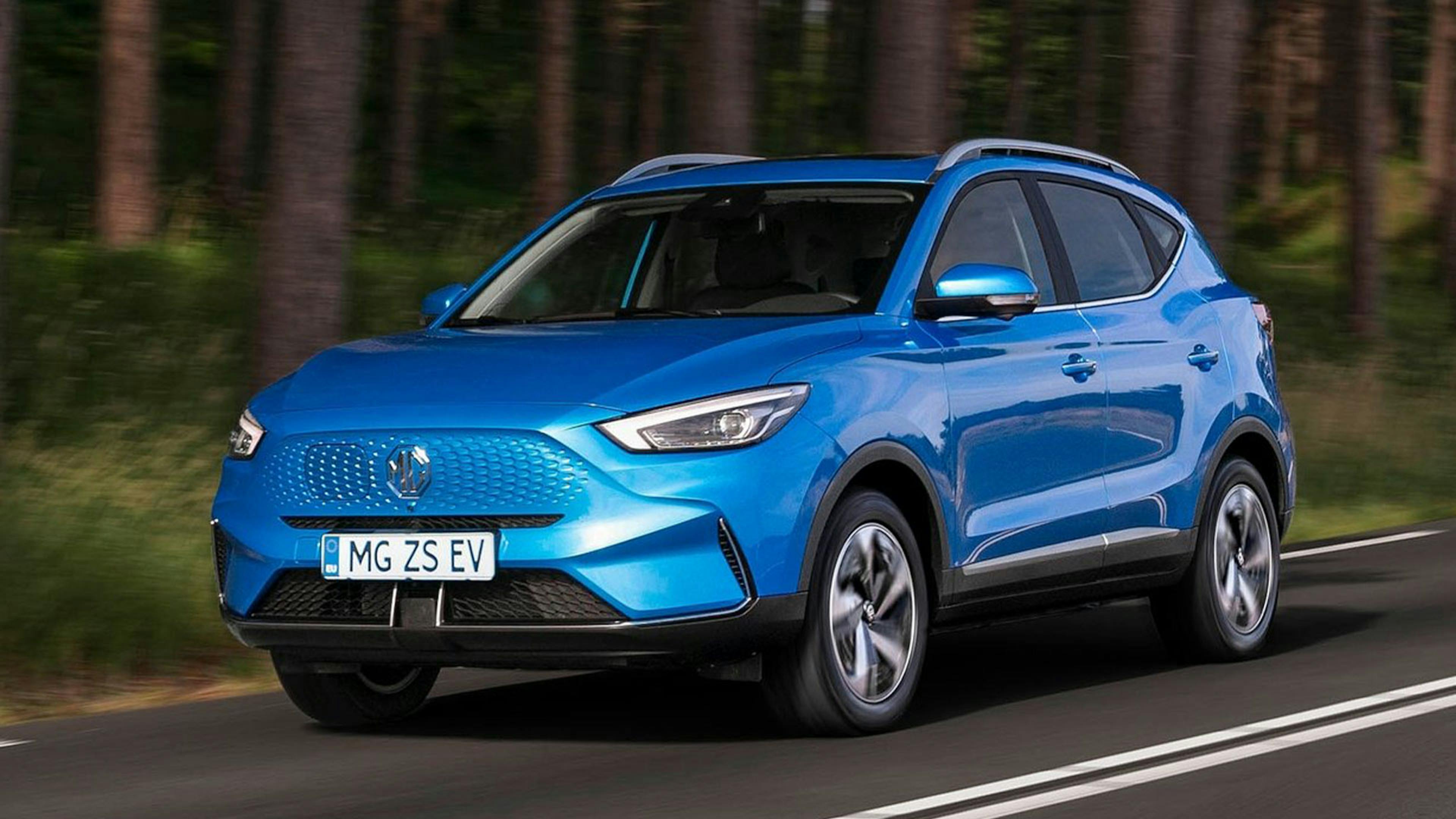 Ein blauer MG ZS EV fährt auf einer Landstraße an einem Wald vorbei.