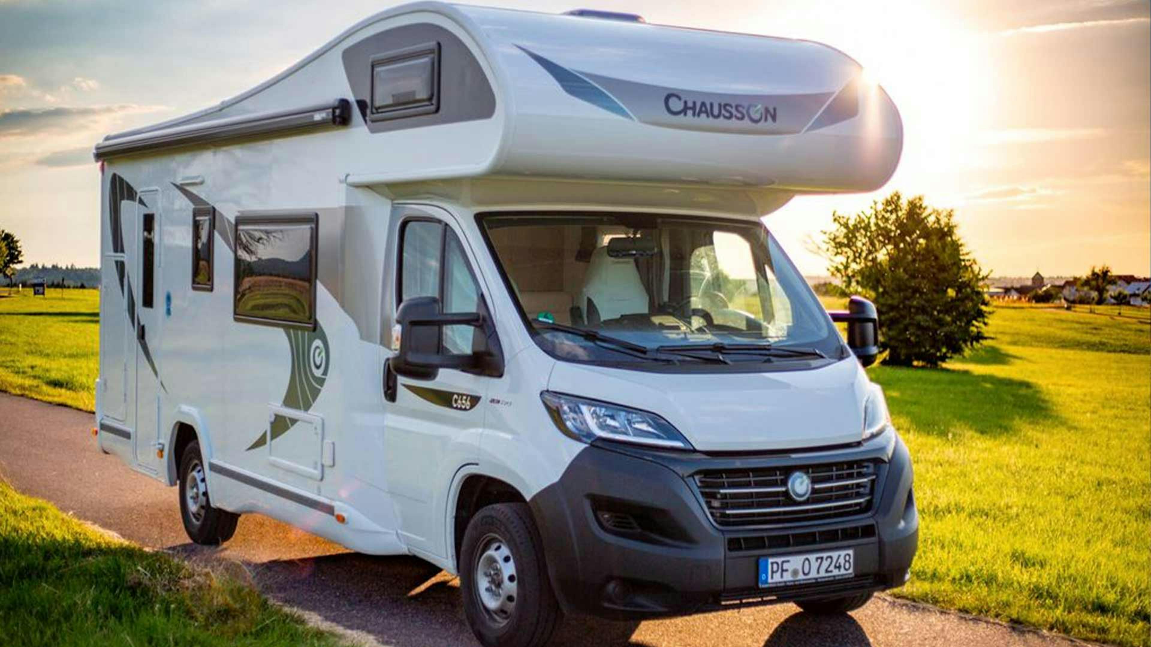 Ein Chausson Wohnmobil aus der C-Serie mit Alkoven steht auf einem Feldweg vor einer Wiese.