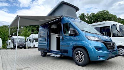 Ein blauer Hymer Free 540 steht mit aufgeklapptem Dach und offener Seitentür auf einem Parkplatz.