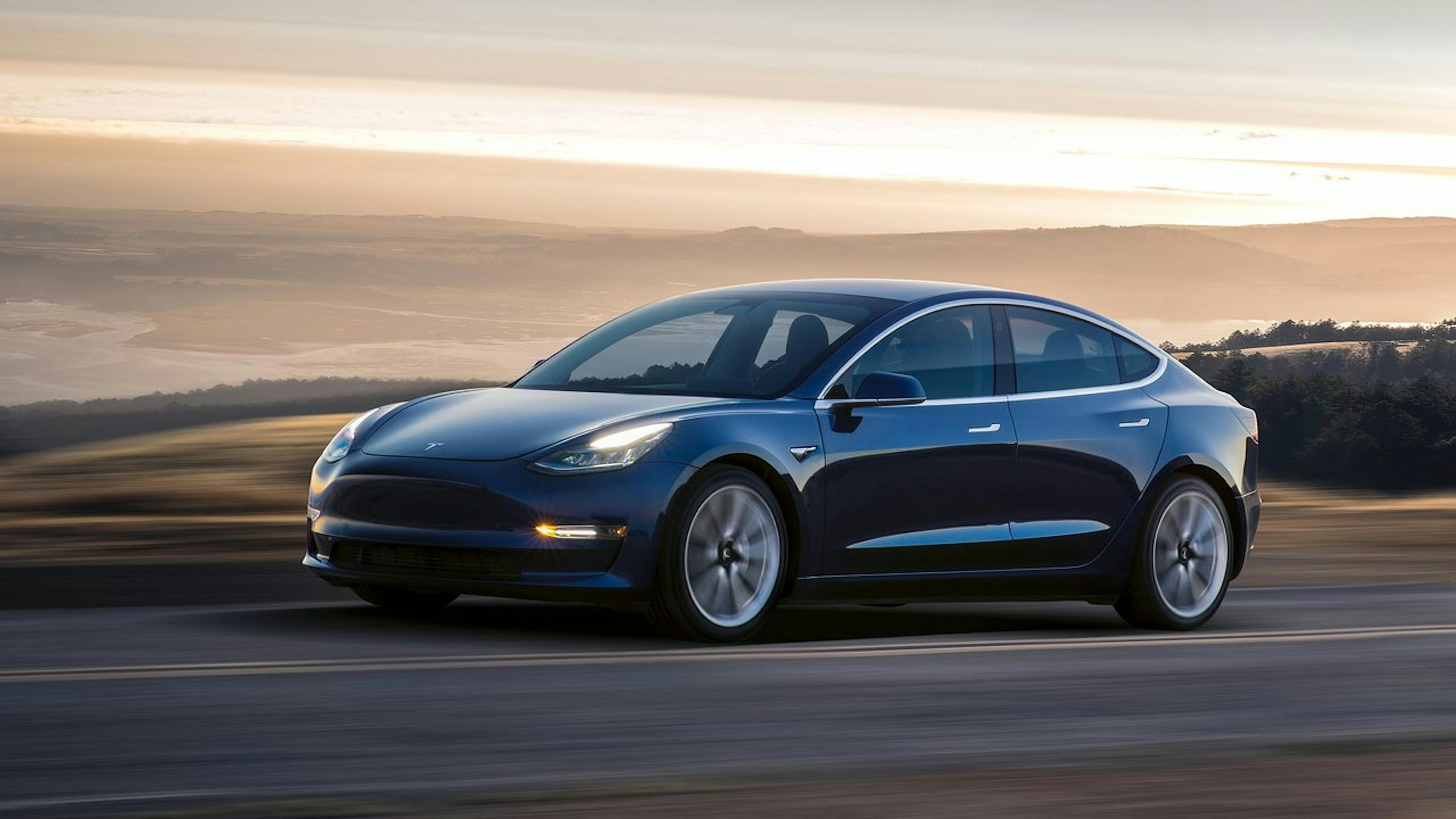 Blauer Tesla Model 3 fährt auf Landstraße