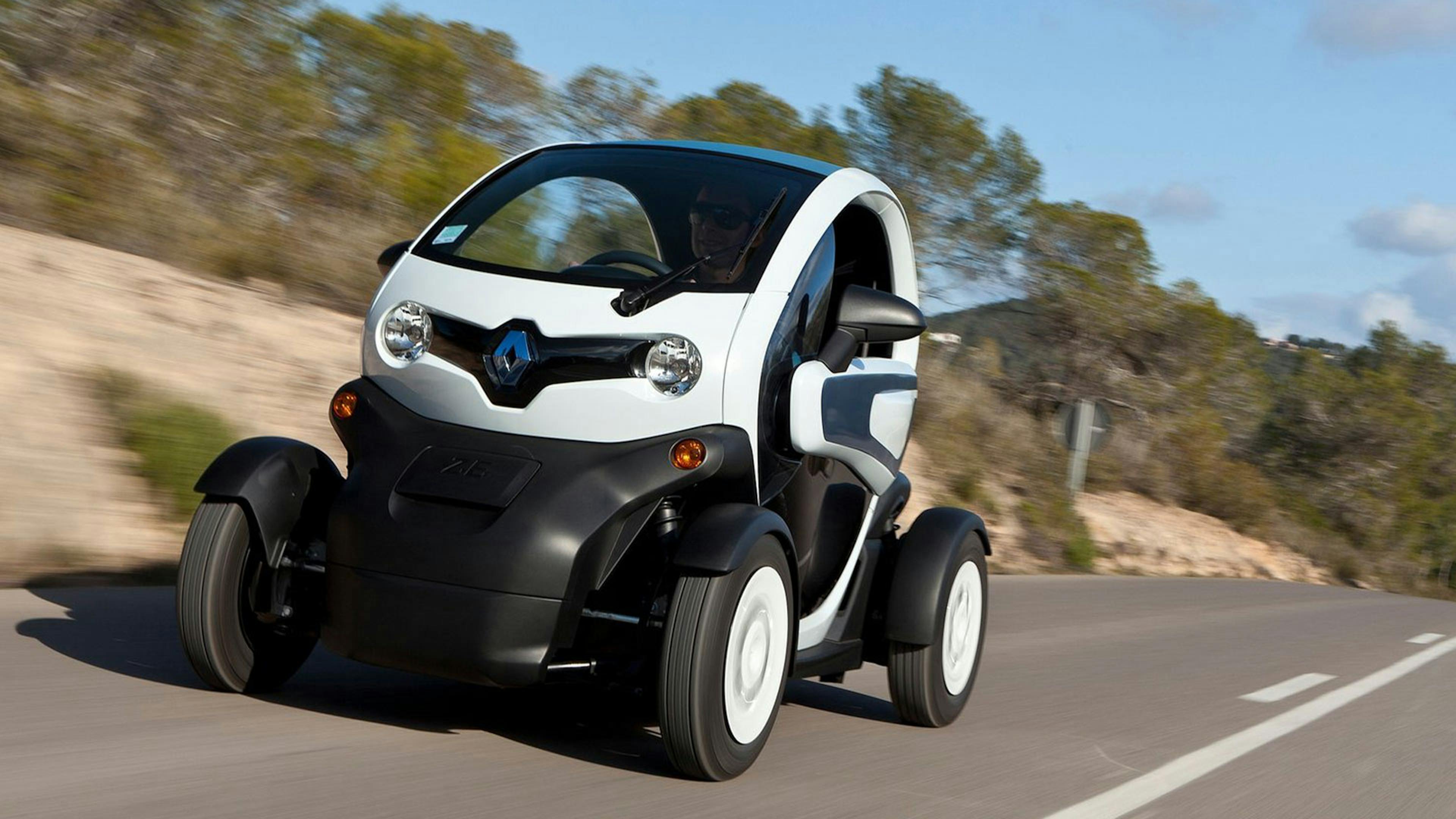 Ein schwarz-weißer Renault Twizy fährt eine Landstraße entlang.