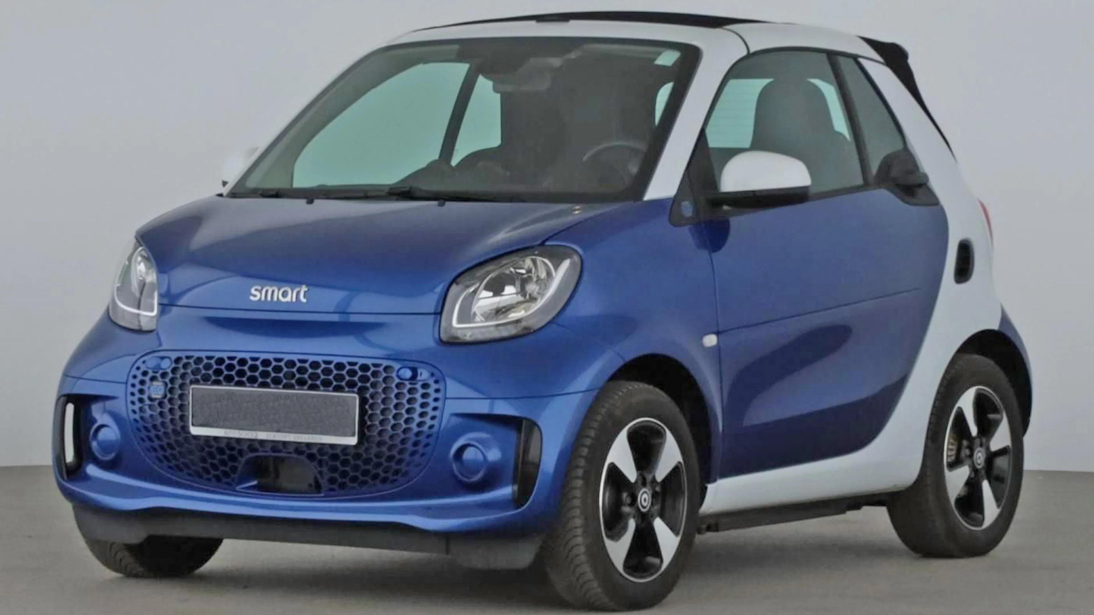 Ein blauer Smart fortwo Zweisitzer steht vor einer grauen Wand.