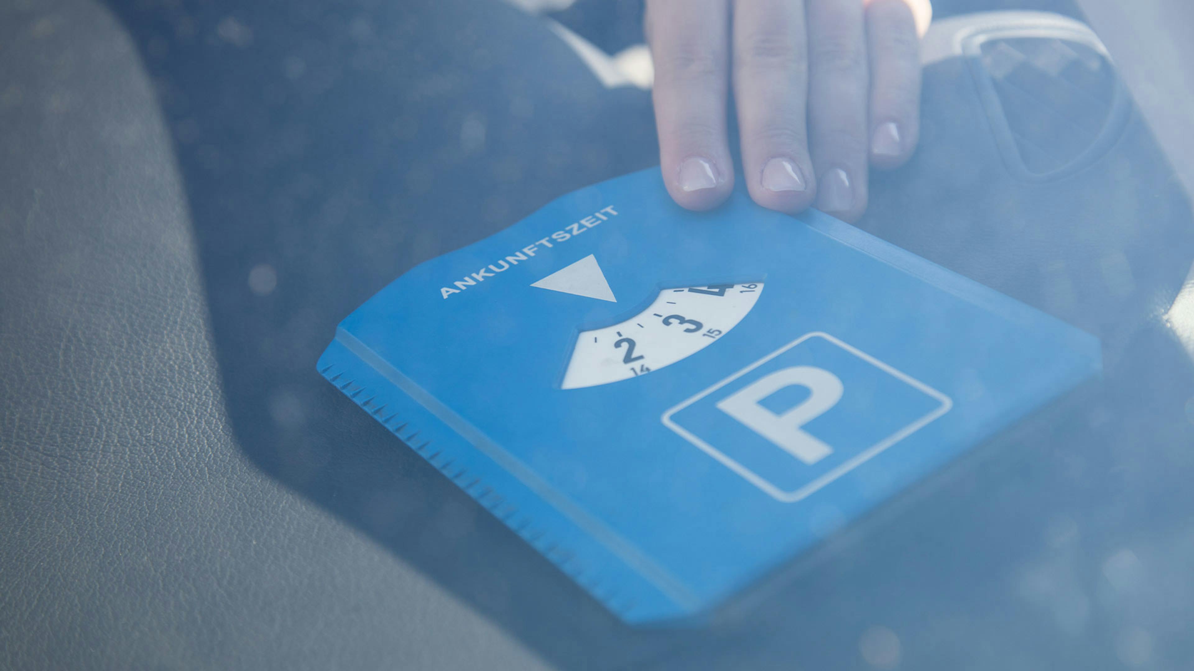 Eine Person legt eine blaue Parkscheibe auf das Handschuhfach eines Pkw.