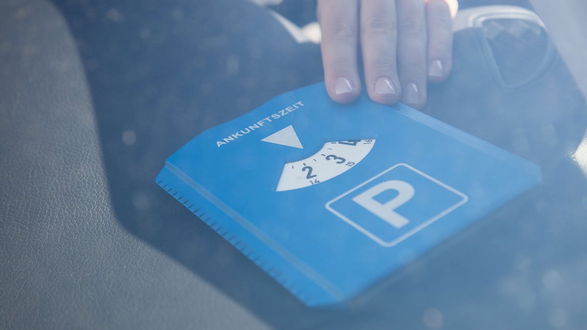 Eine Person legt eine blaue Parkscheibe auf das Handschuhfach eines Pkw.