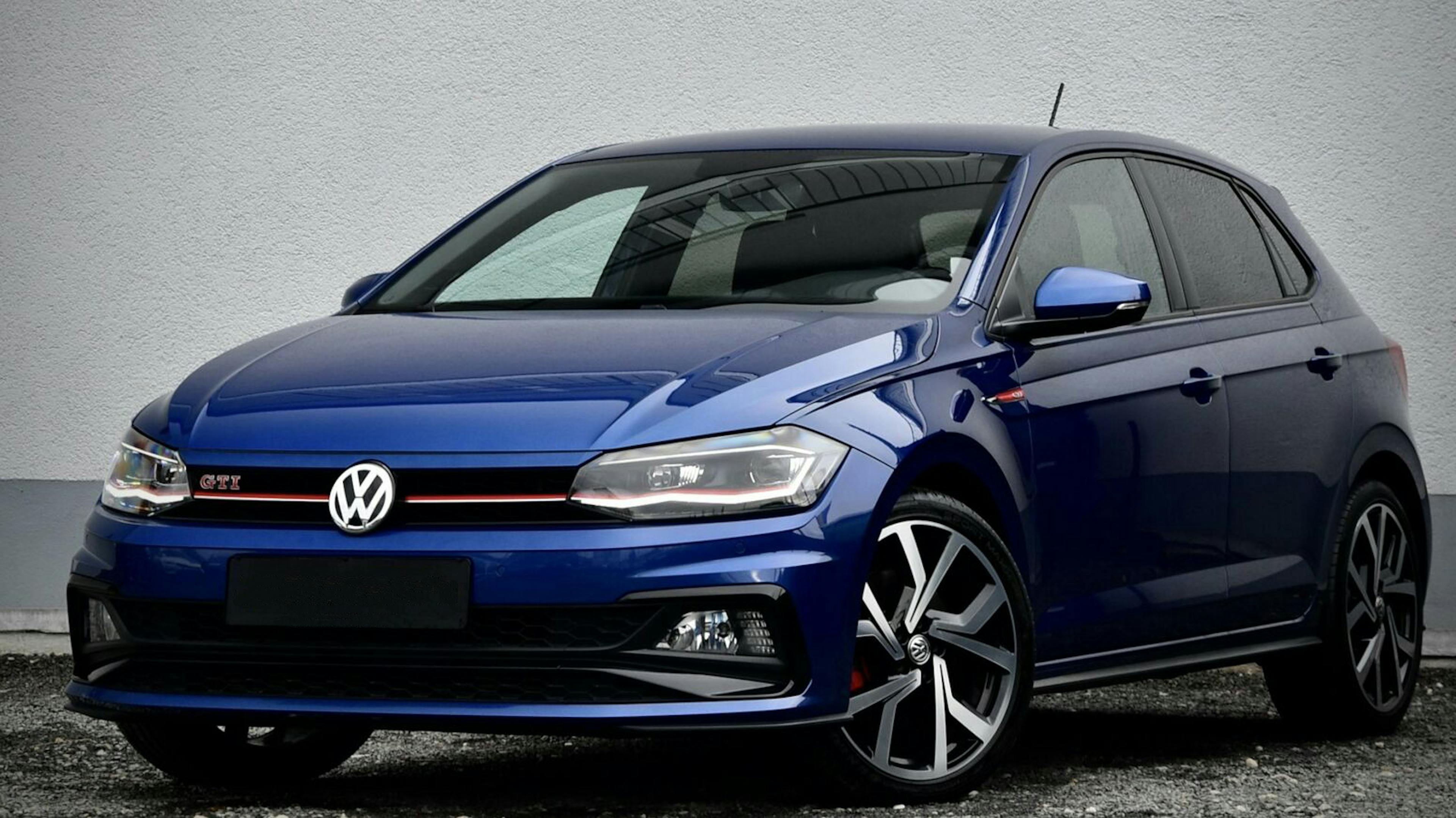 Ein blauer VW Polo steht vor einer grauen Wand.