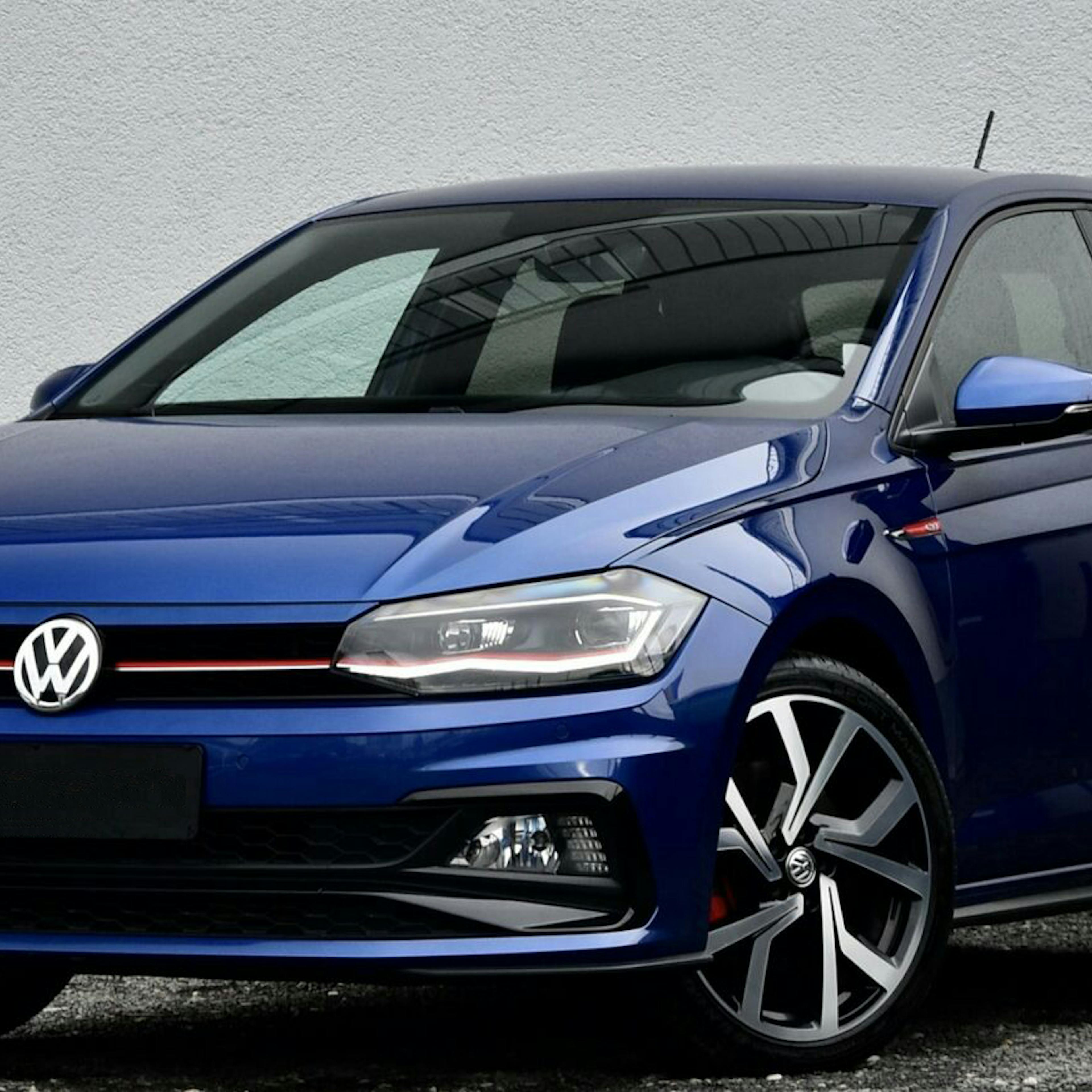 Ein blauer VW Polo steht vor einer grauen Wand.
