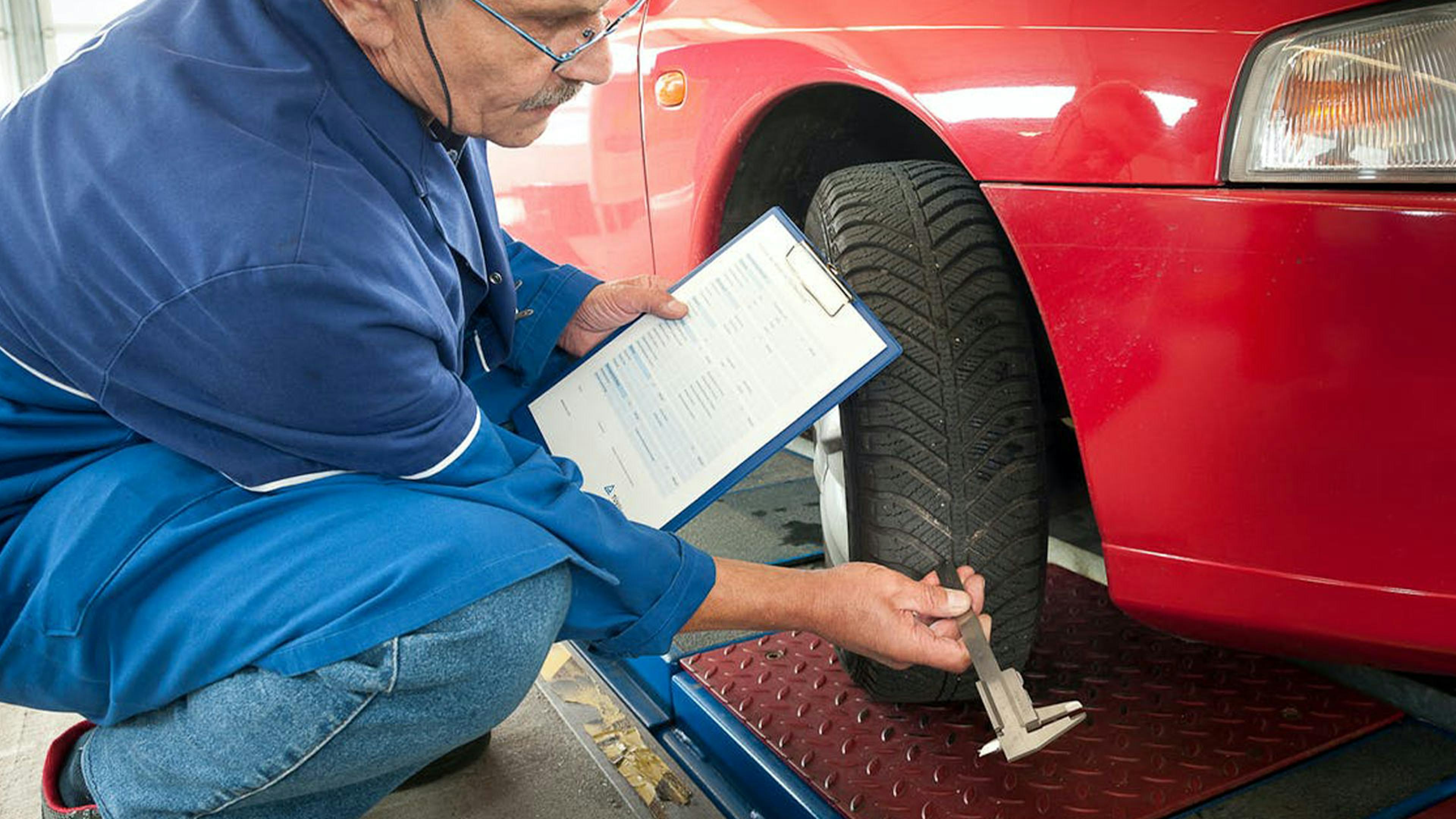 Ein Mechaniker des TÜV Rheinland misst die Profiltiefe an einem Autoreifen.