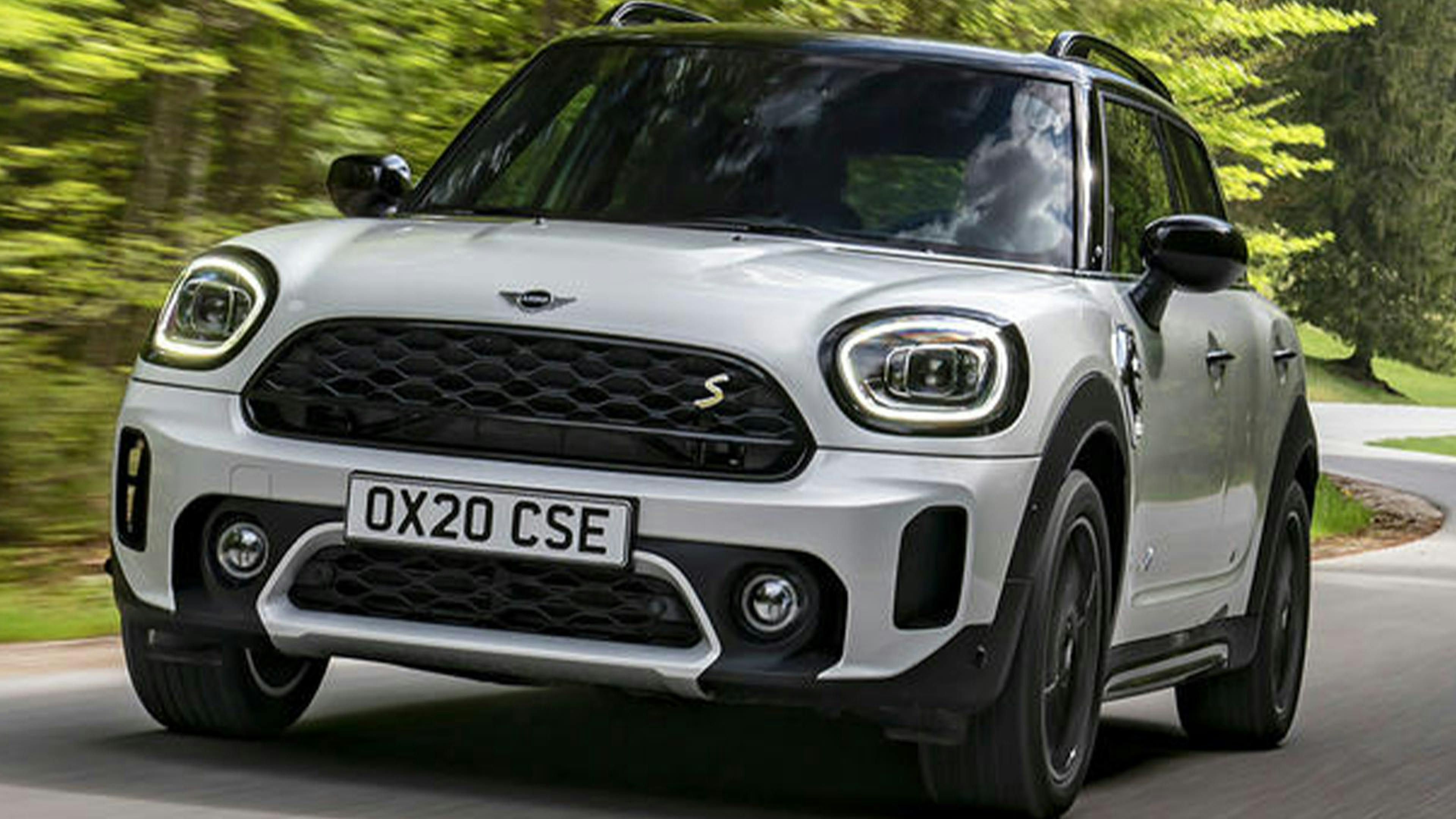 Ein silberner Mini Countryman Hybrid-SUV fährt eine Straße entlang an Bäumen vorbei