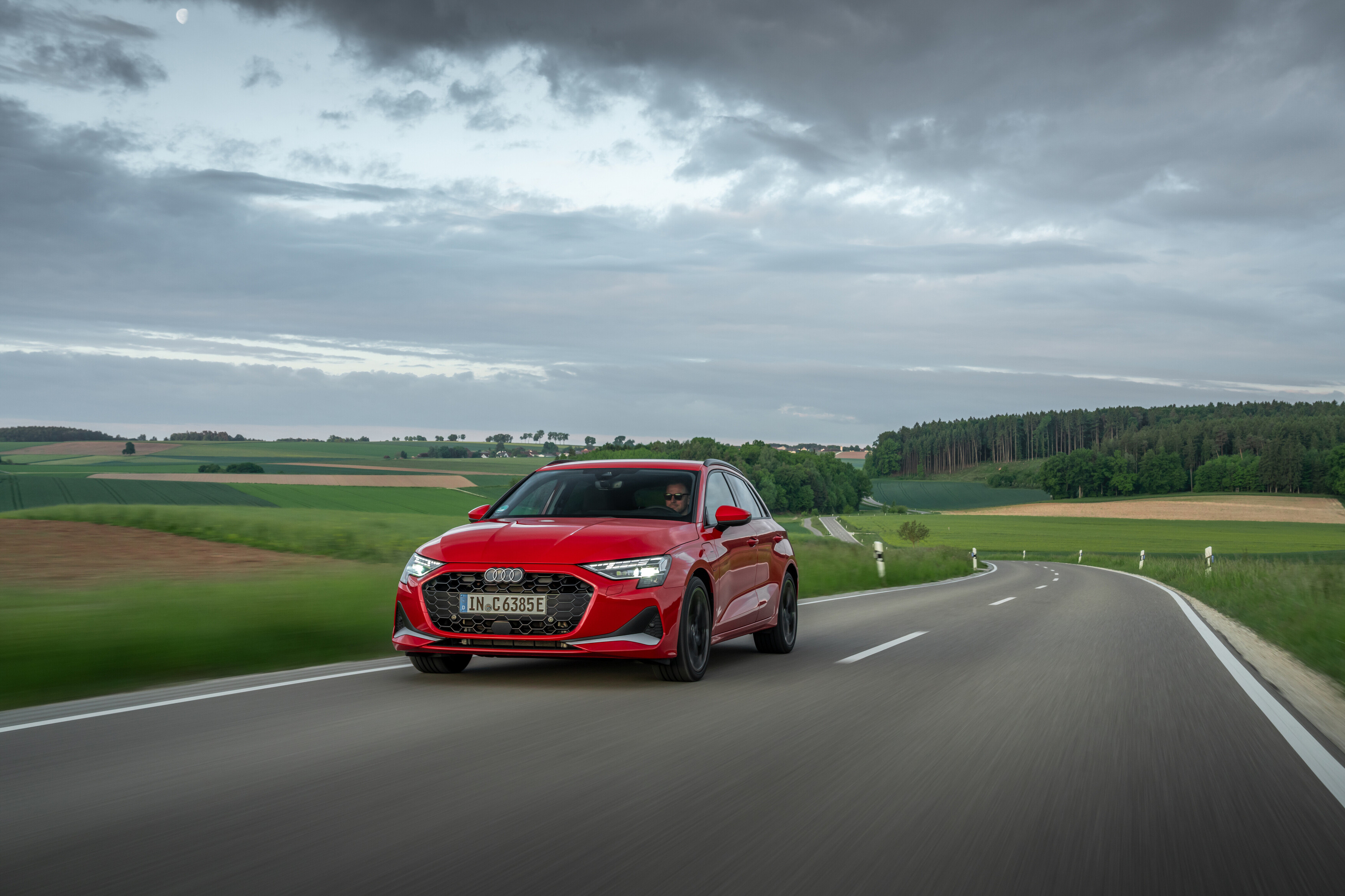 Roter Audi A3 Sportback fährt auf einer Landstraße vor Hügeln und Gewitterhimmel.