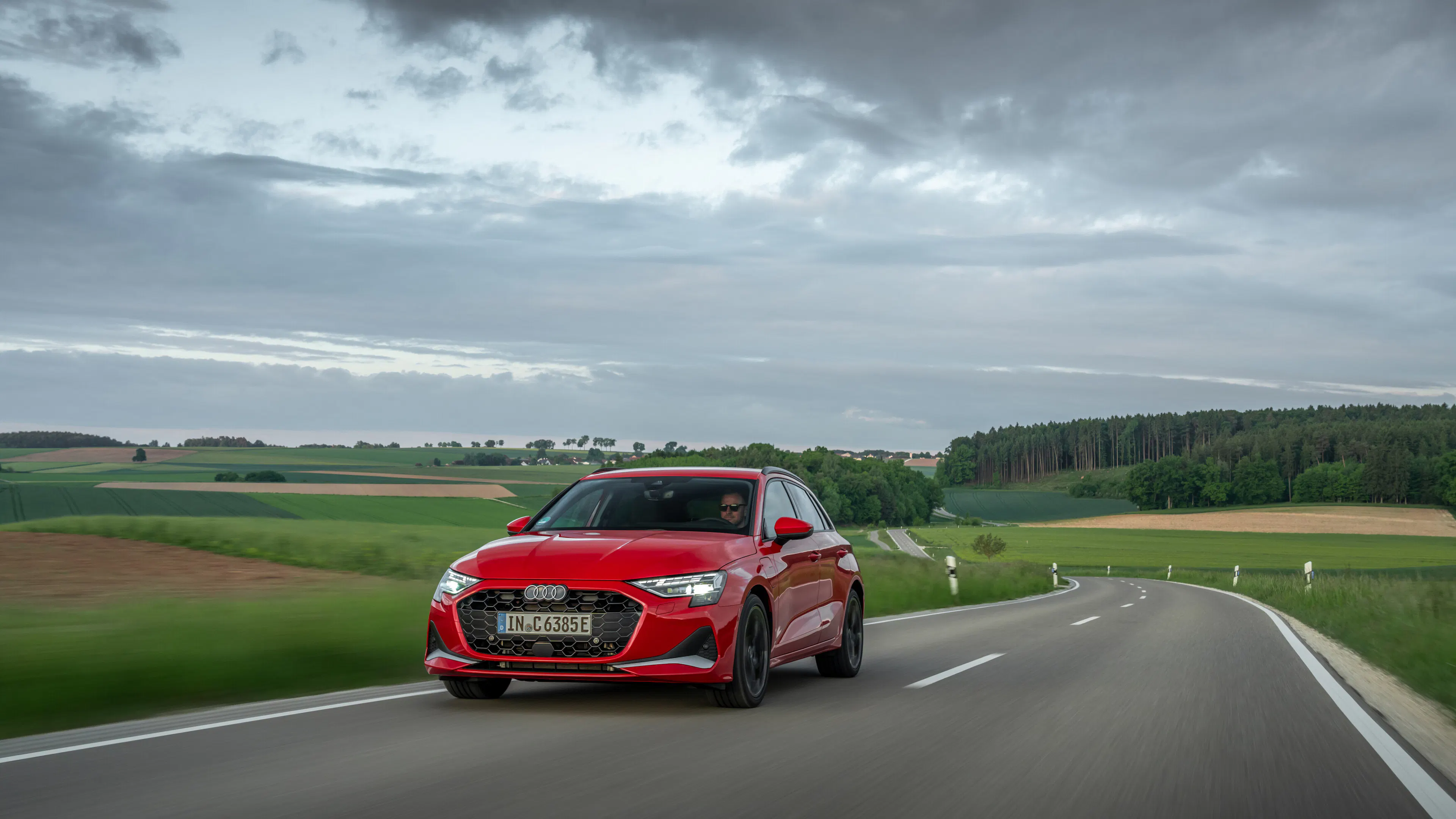 Roter Audi A3 Sportback fährt auf einer Landstraße vor Hügeln und Gewitterhimmel.