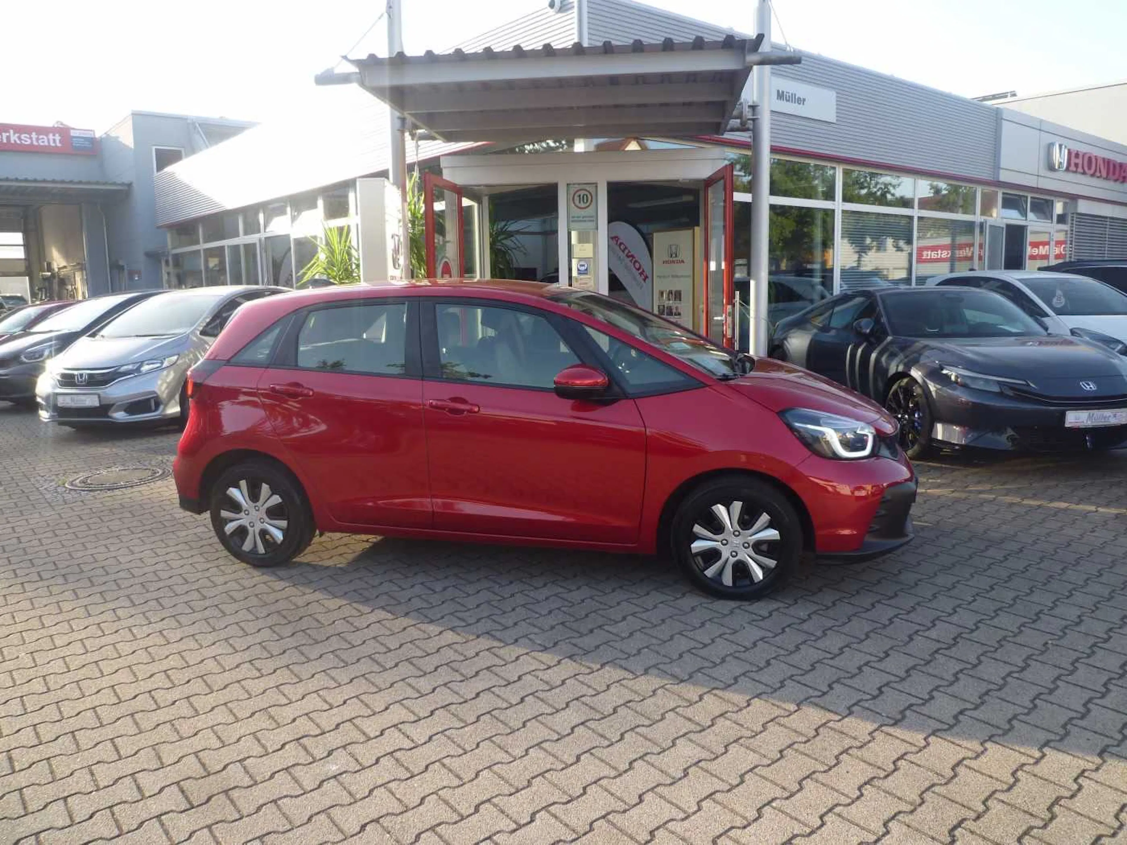Ein roter Honda Jazz steht auf einer gepflasterten Fläche.