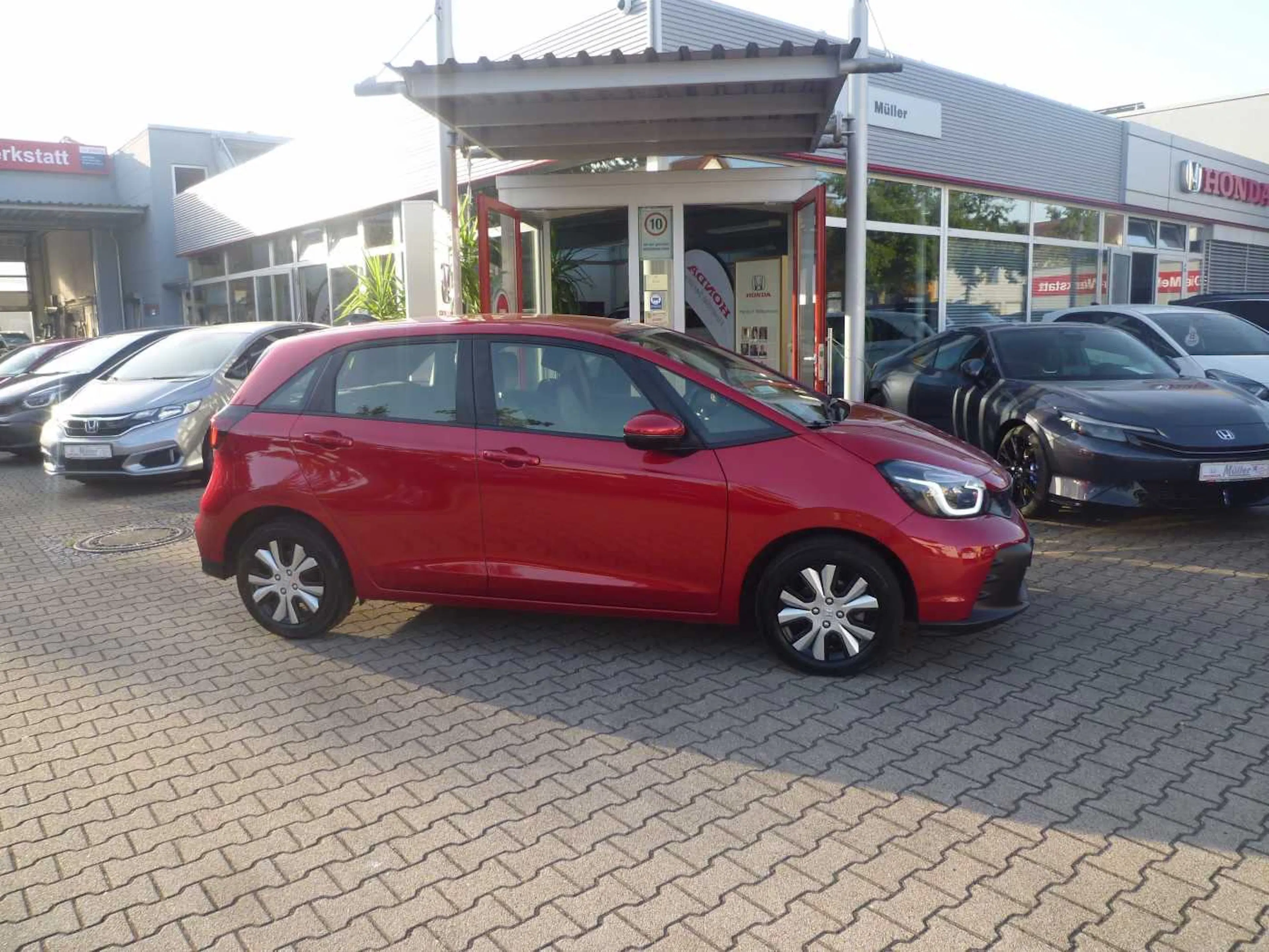 Ein roter Honda Jazz steht auf einer gepflasterten Fläche.