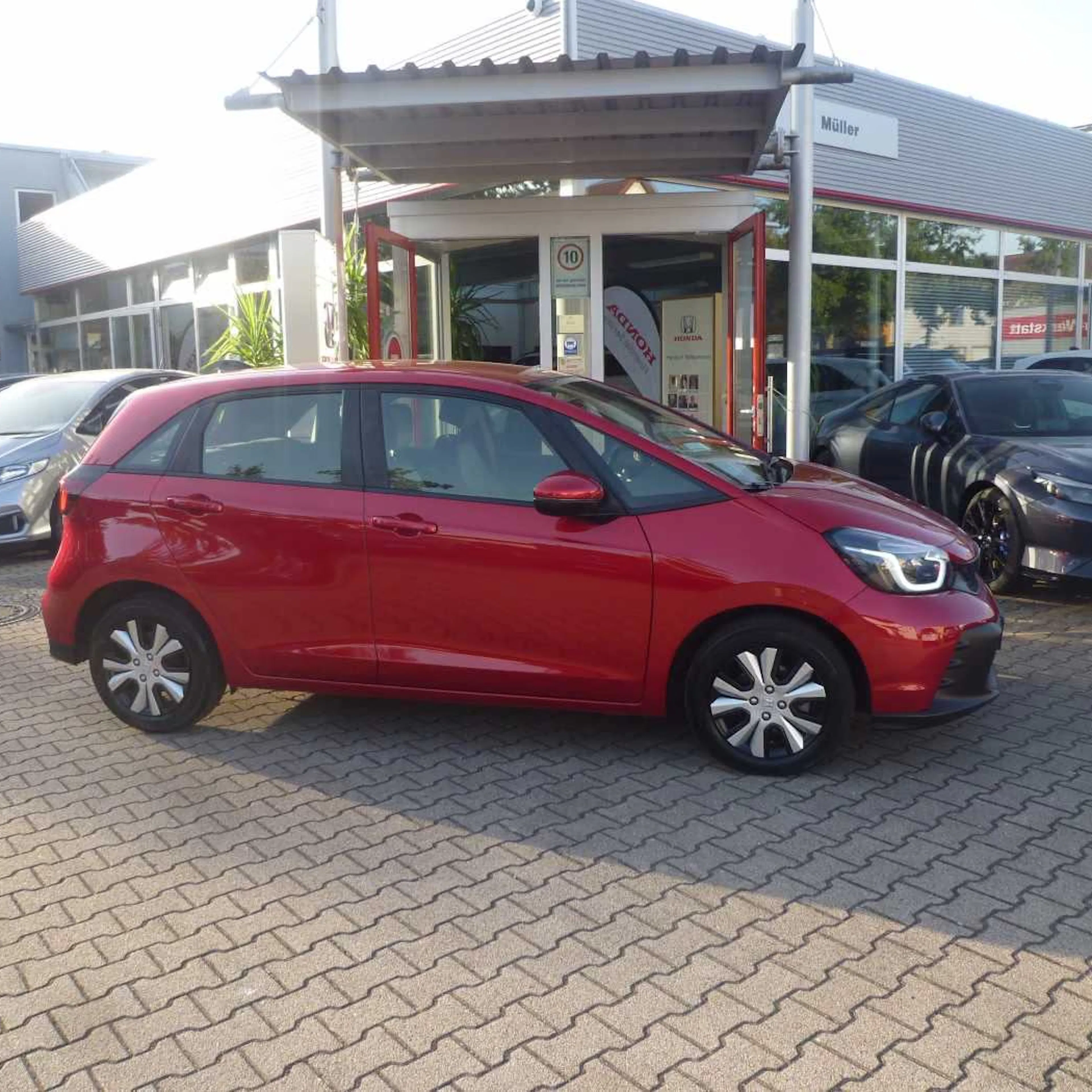 Ein roter Honda Jazz steht auf einer gepflasterten Fläche.