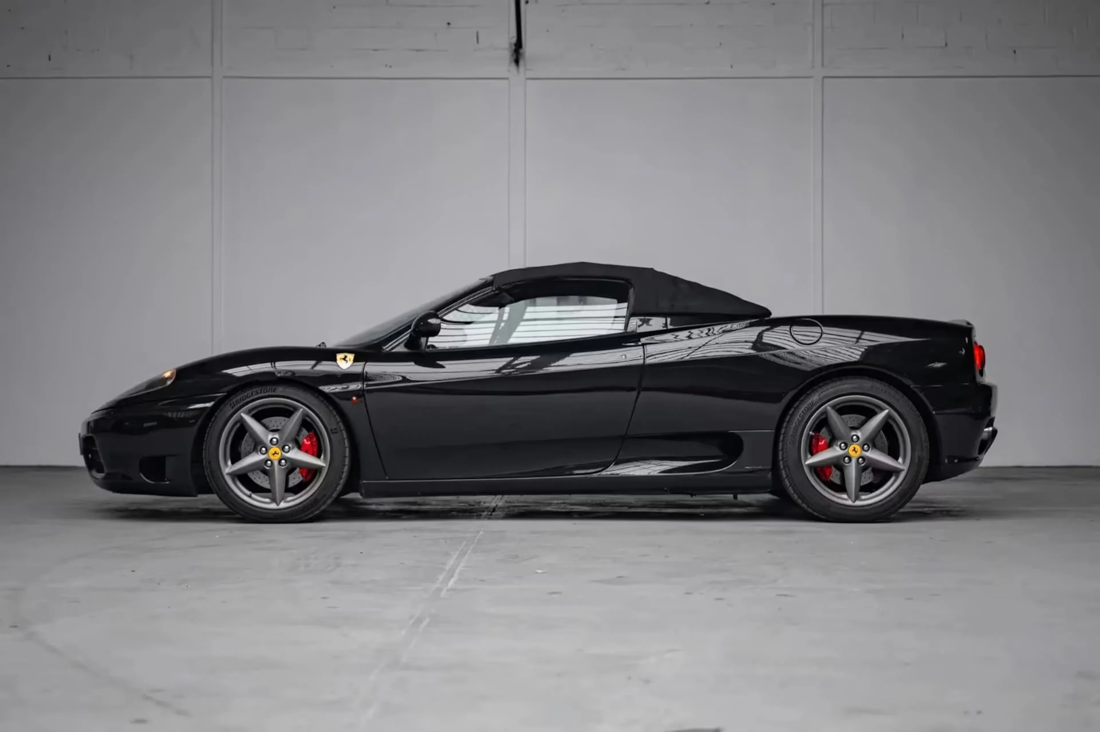 Ein schwarzer Ferrari 360 Modena steht vor einer Betonwand.