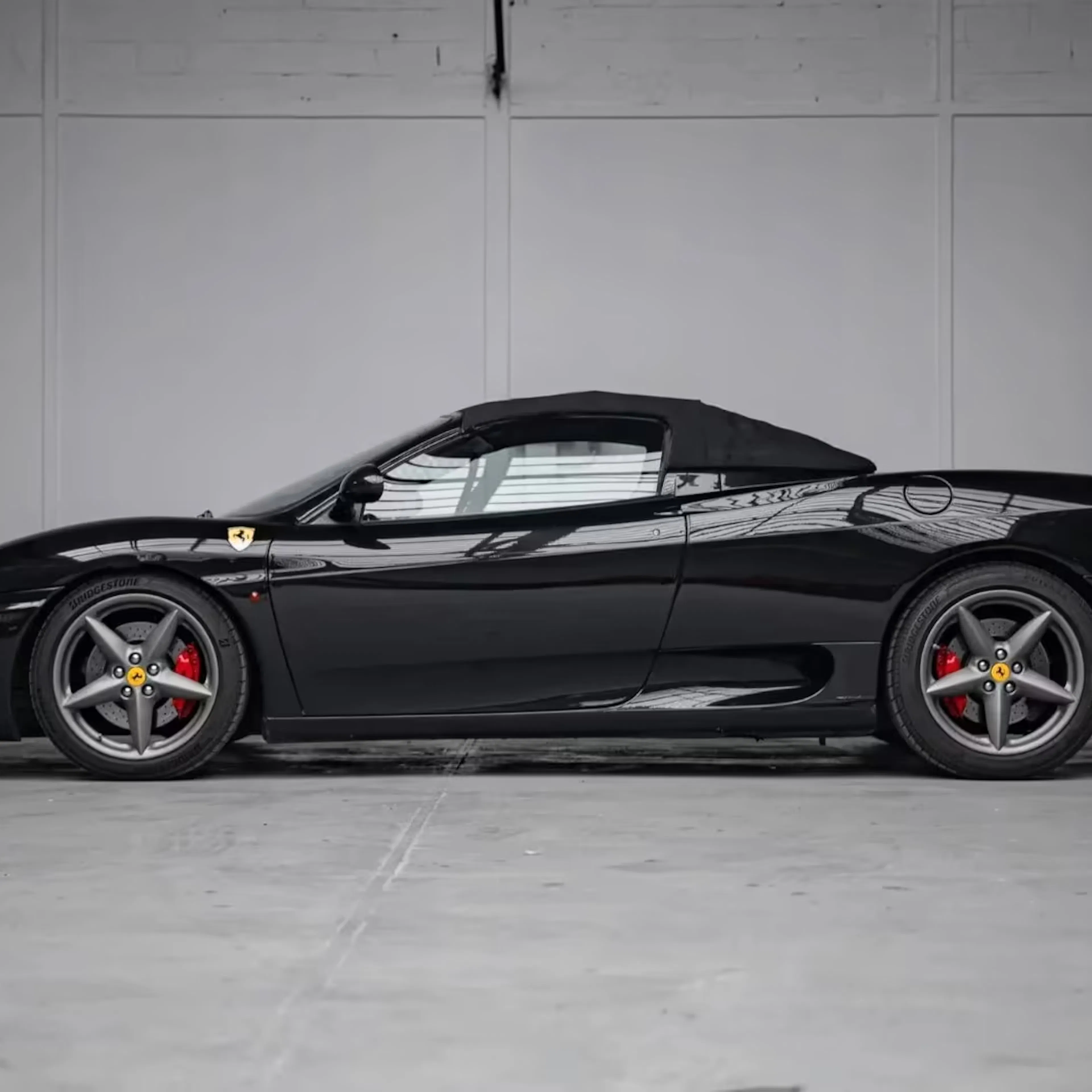 Ein schwarzer Ferrari 360 Modena steht vor einer Betonwand.