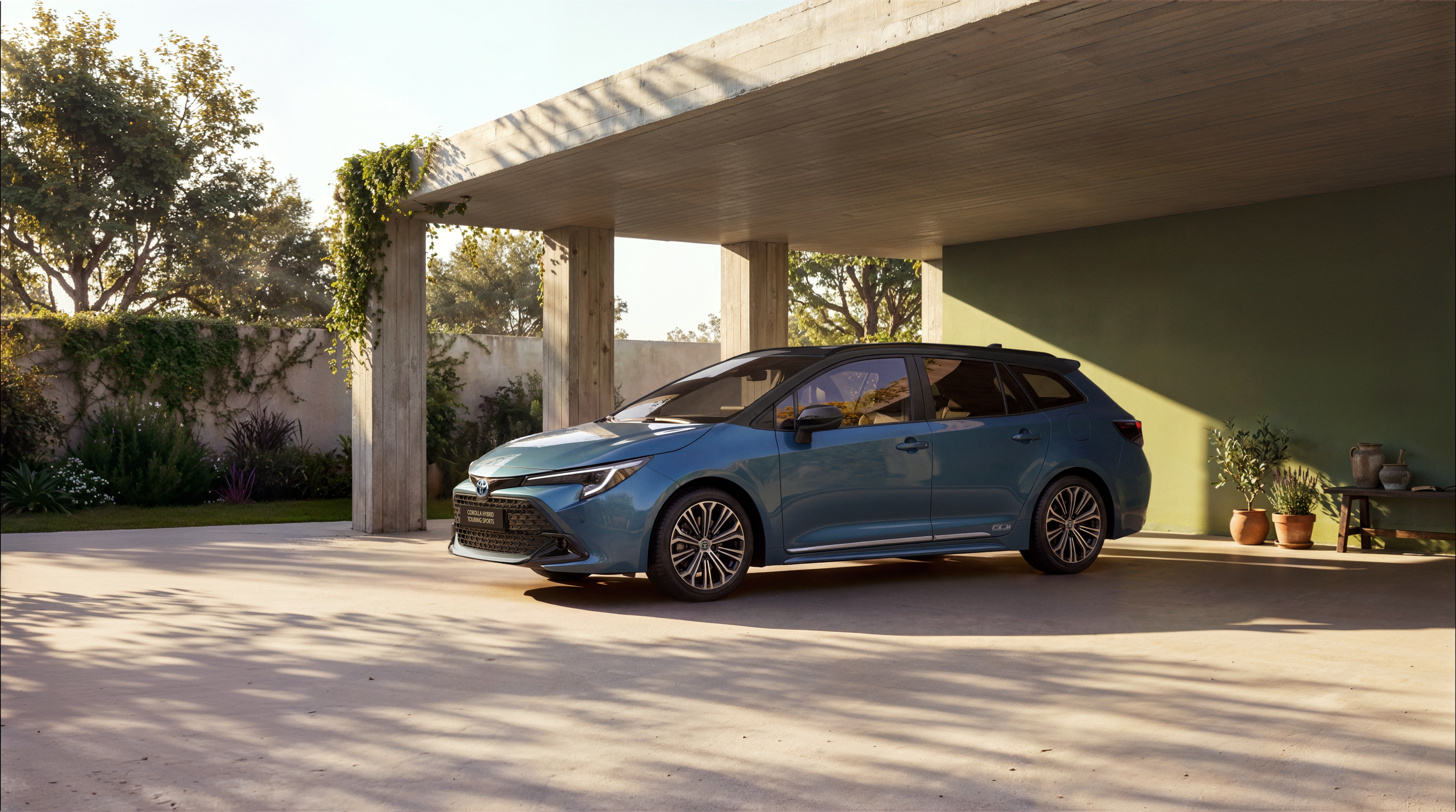 Blauer Toyota Corolla Touring Sports mit schwarzem Dach steht unter einem Betonvordach vor einer grünen Wand.