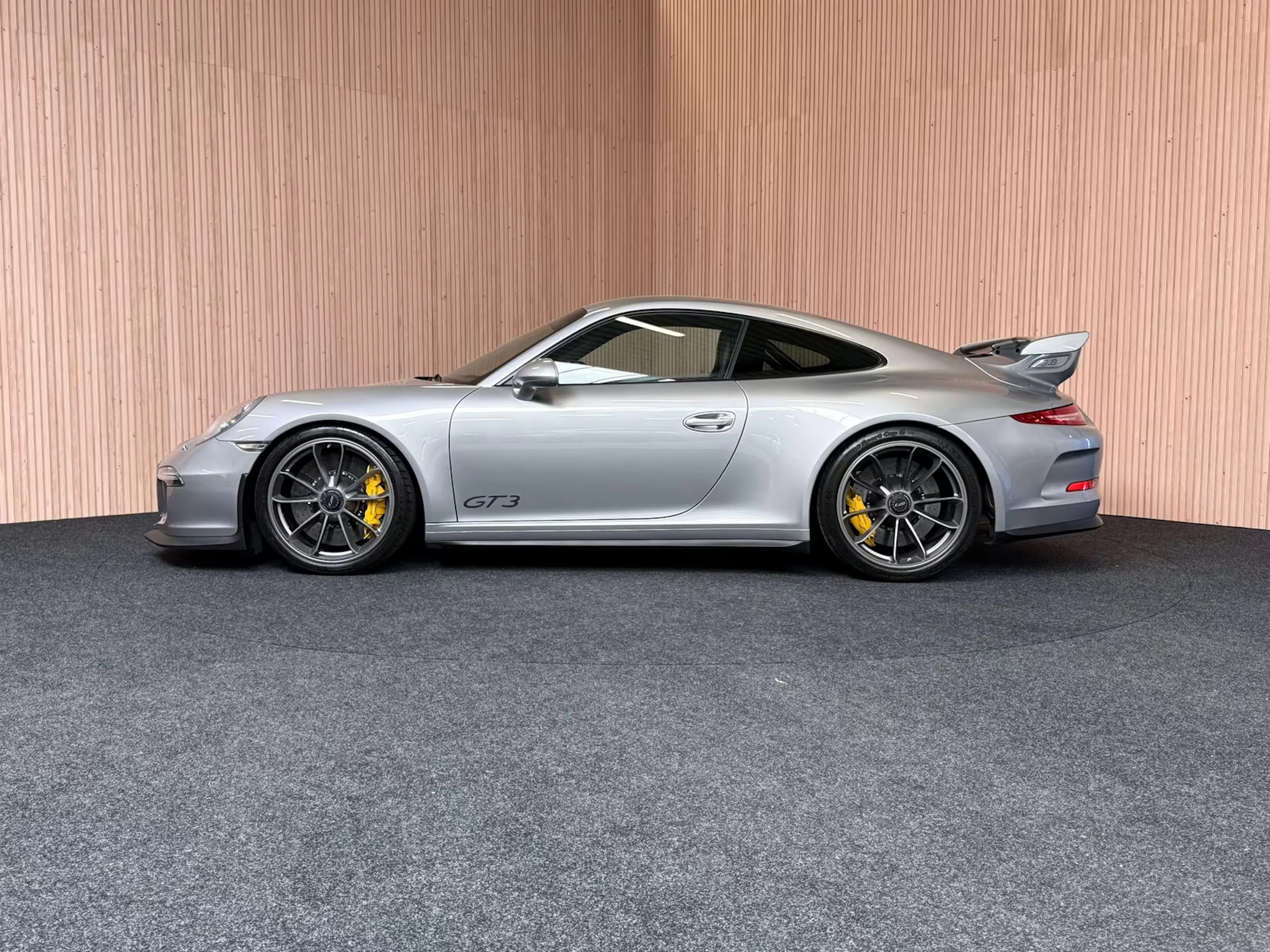 Silberner Porsche 911 GT3 steht vor Holzwand auf grauem Teppich