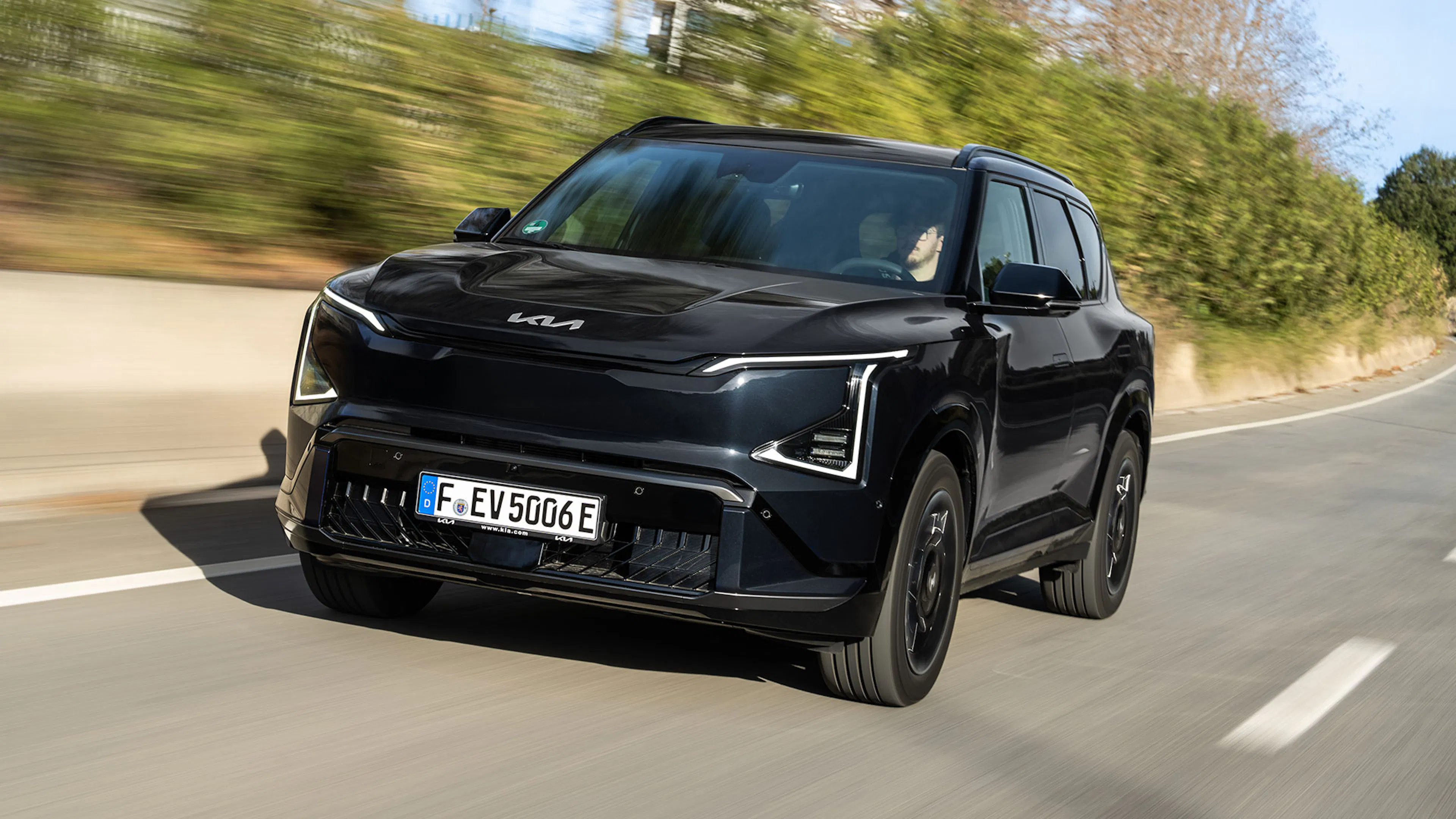 Schwarzer Kia EV5 in Front-Dreiviertelansicht auf einer kurvigen Landstraße.