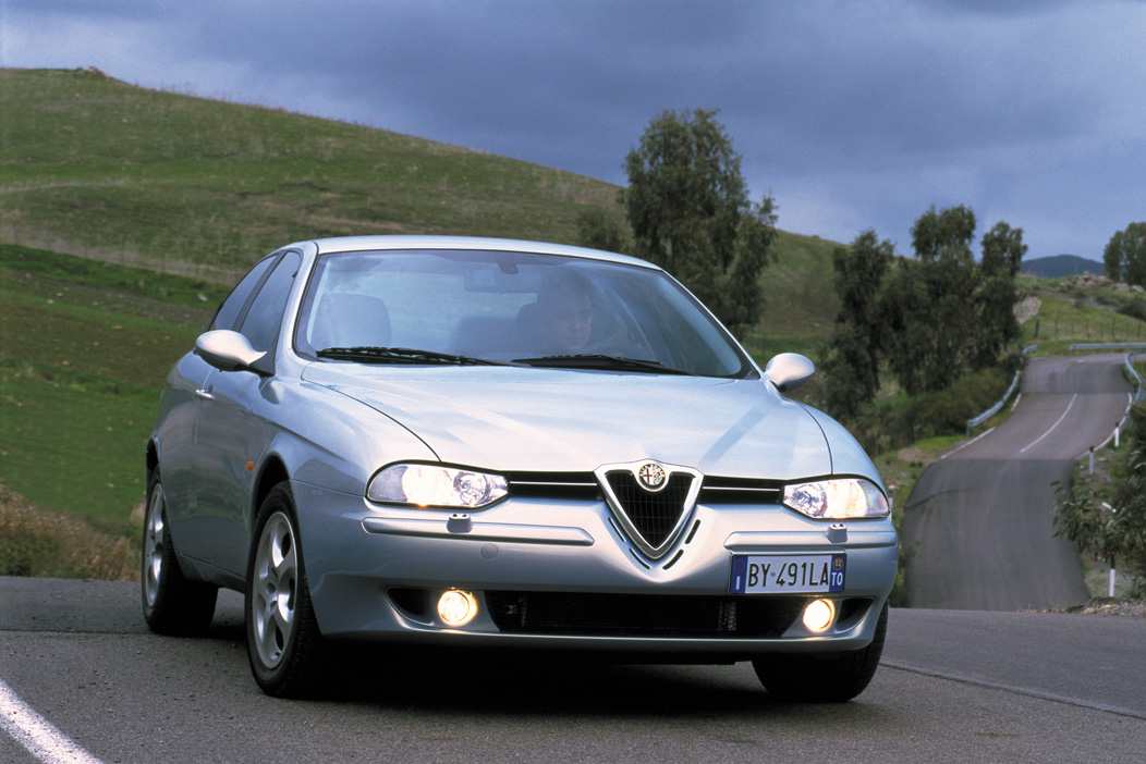 Silberner Alfa Romeo 156 Serie I (1997–2003) in der Dreiviertel-Frontansicht auf einer Landstraße.