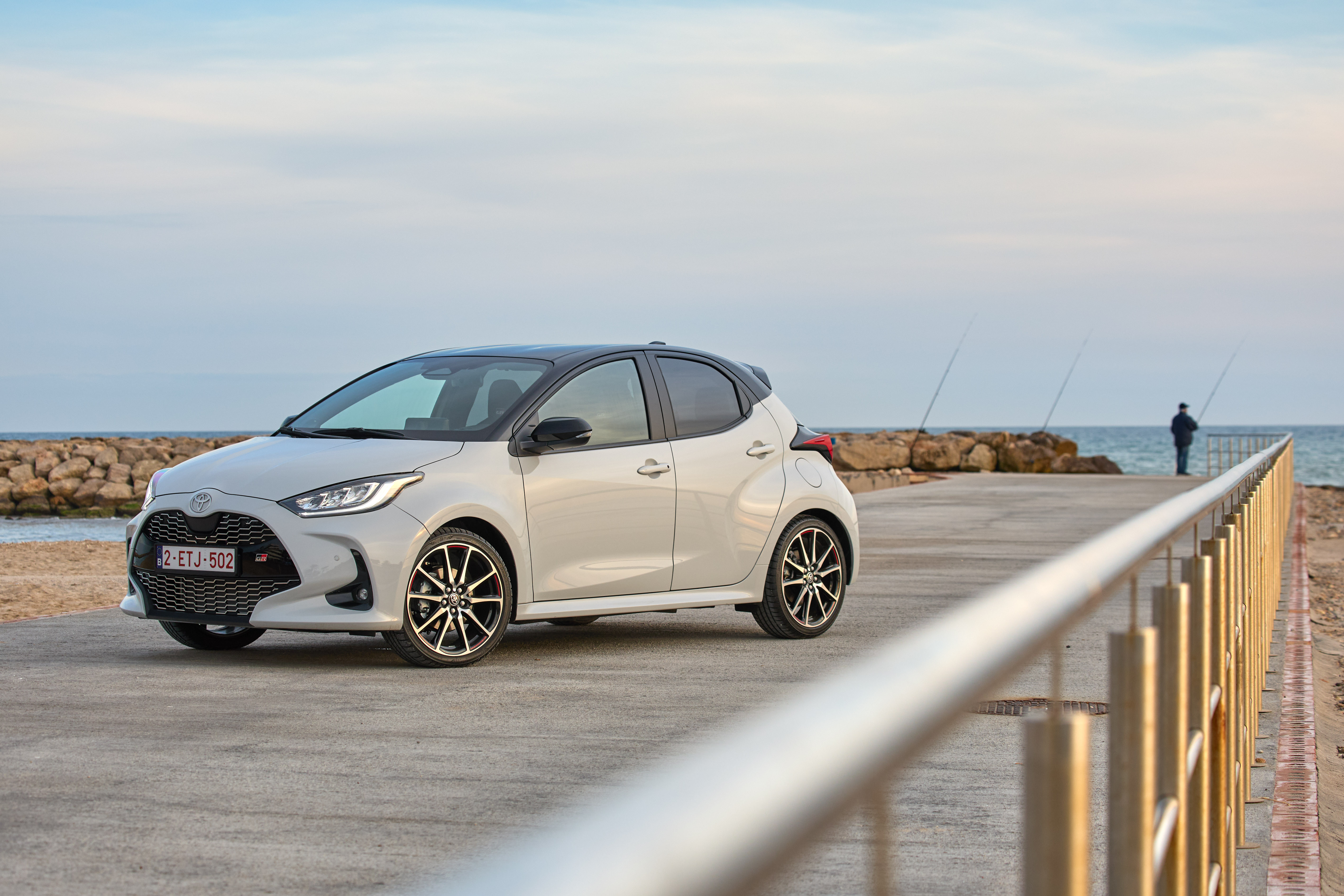 Weißer Toyota Yaris mit schwarzem Dach steht schräg von vorn gesehen auf einer Mole am Meer.