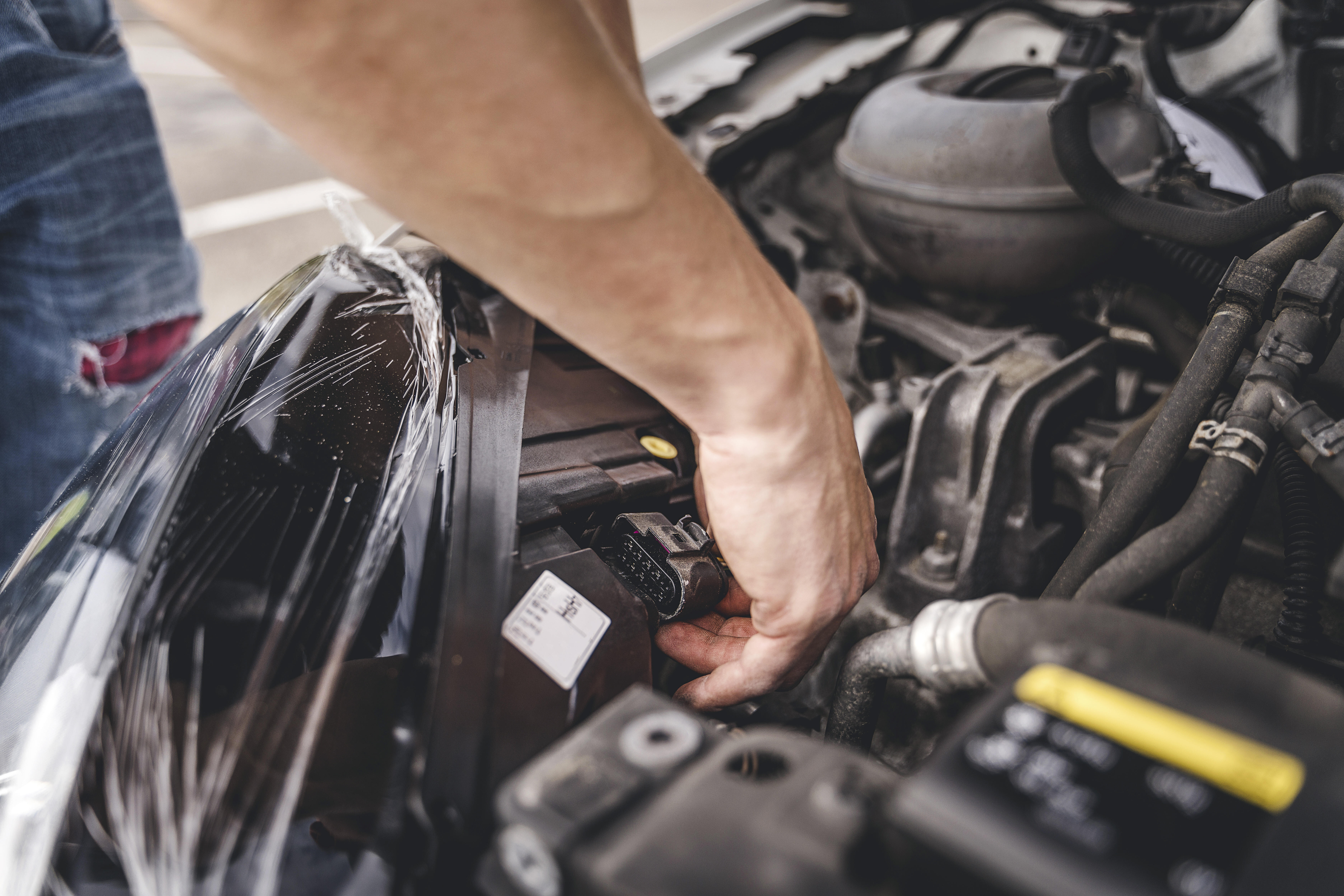 Inspektion: Eine Hand greift in den Motorraum eines Autos und prüft einen elektrischen Stecker.