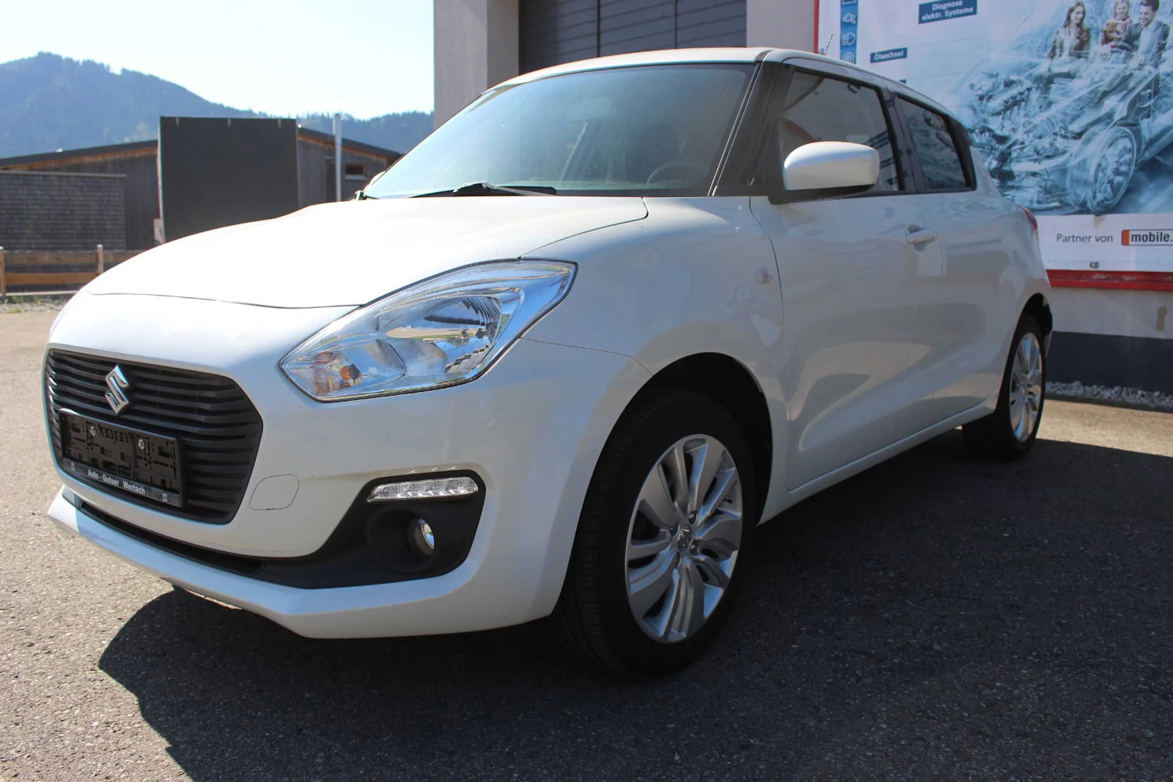 Ein weißer Suzuki Swift steht vor einem mobile.de-Plakat.
