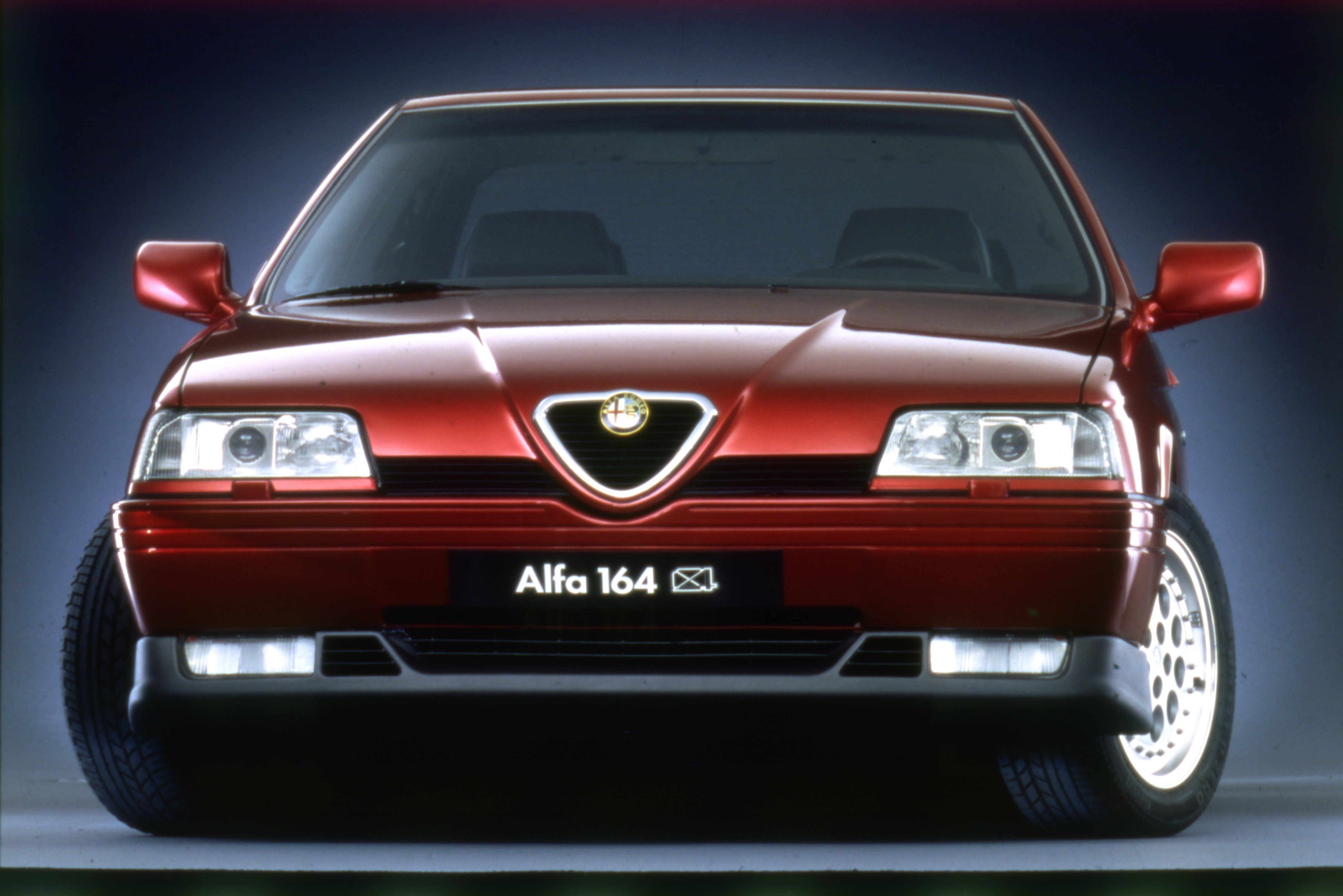 Ein dunkelroter Alfa Romeo 164 steht vor einem dunklen Hintergrund.