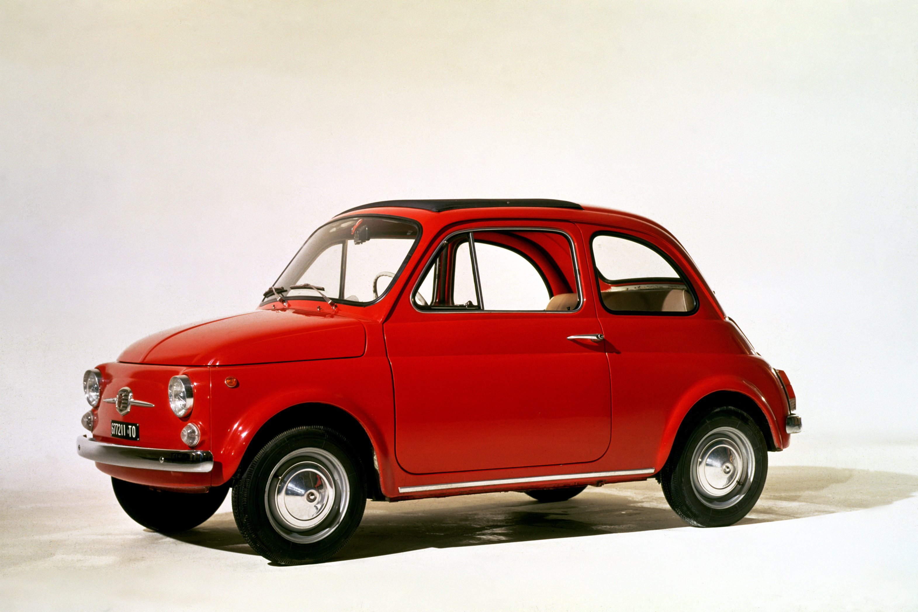 Roter Fiat Nuova 500 F mit geöffnetem Faltdach in seitlicher Studioaufnahme vor weißem Hintergrund.