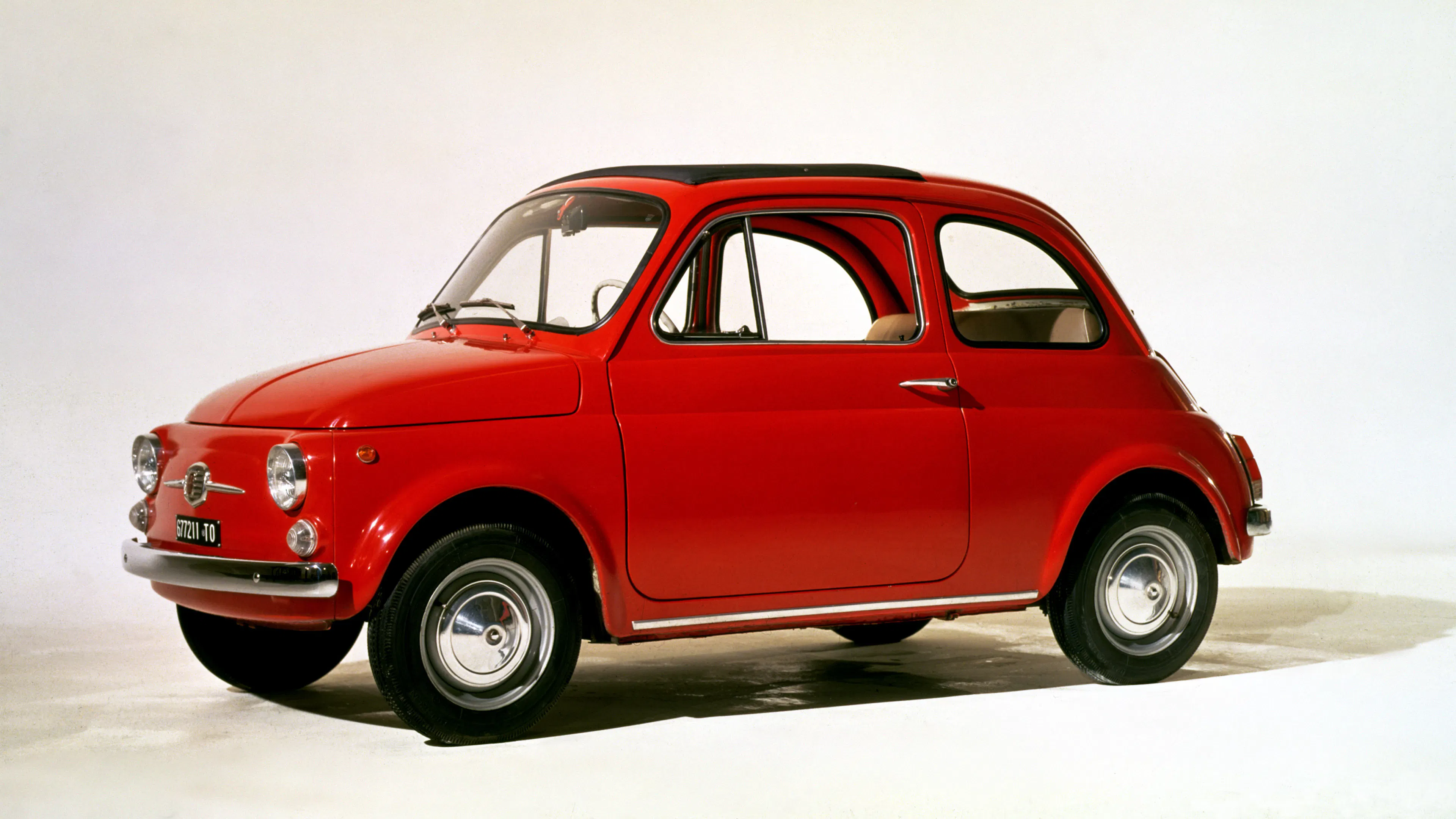 Roter Fiat Nuova 500 F mit geöffnetem Faltdach in seitlicher Studioaufnahme vor weißem Hintergrund.