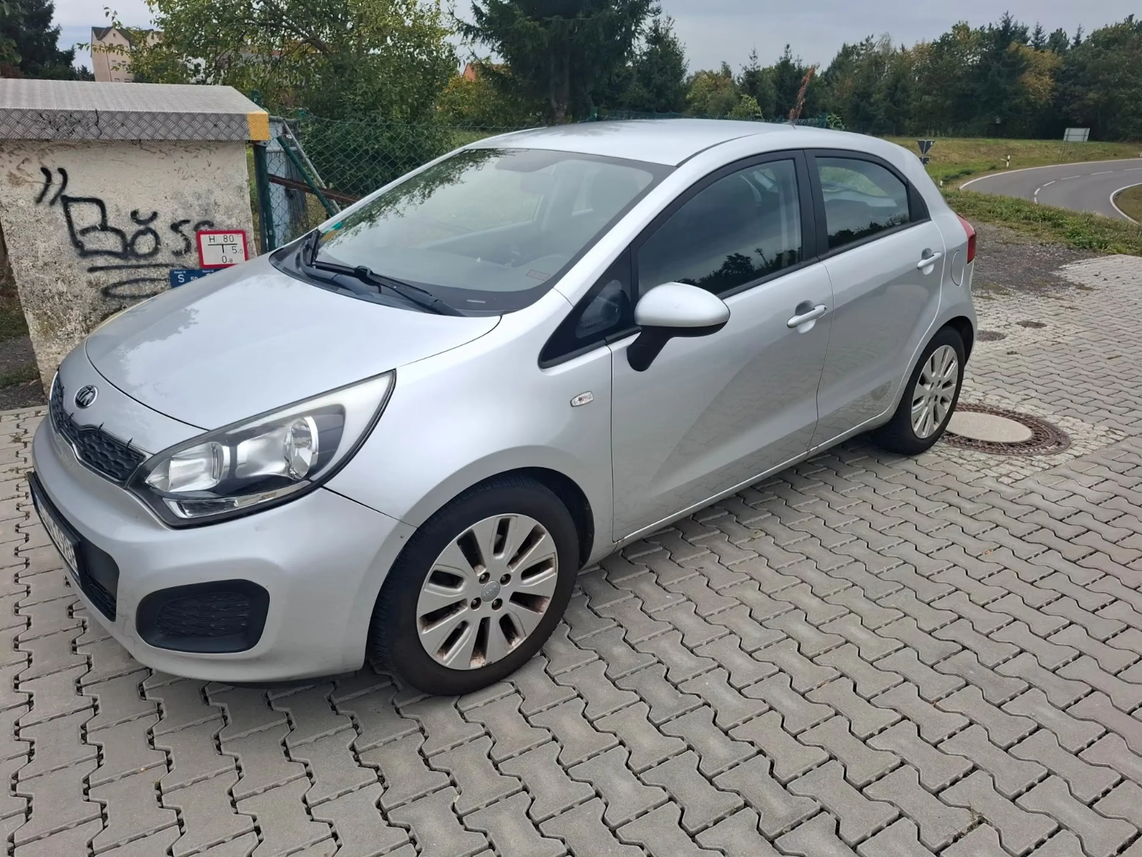 Silberner Kia Rio steht auf gepflastertem Platz