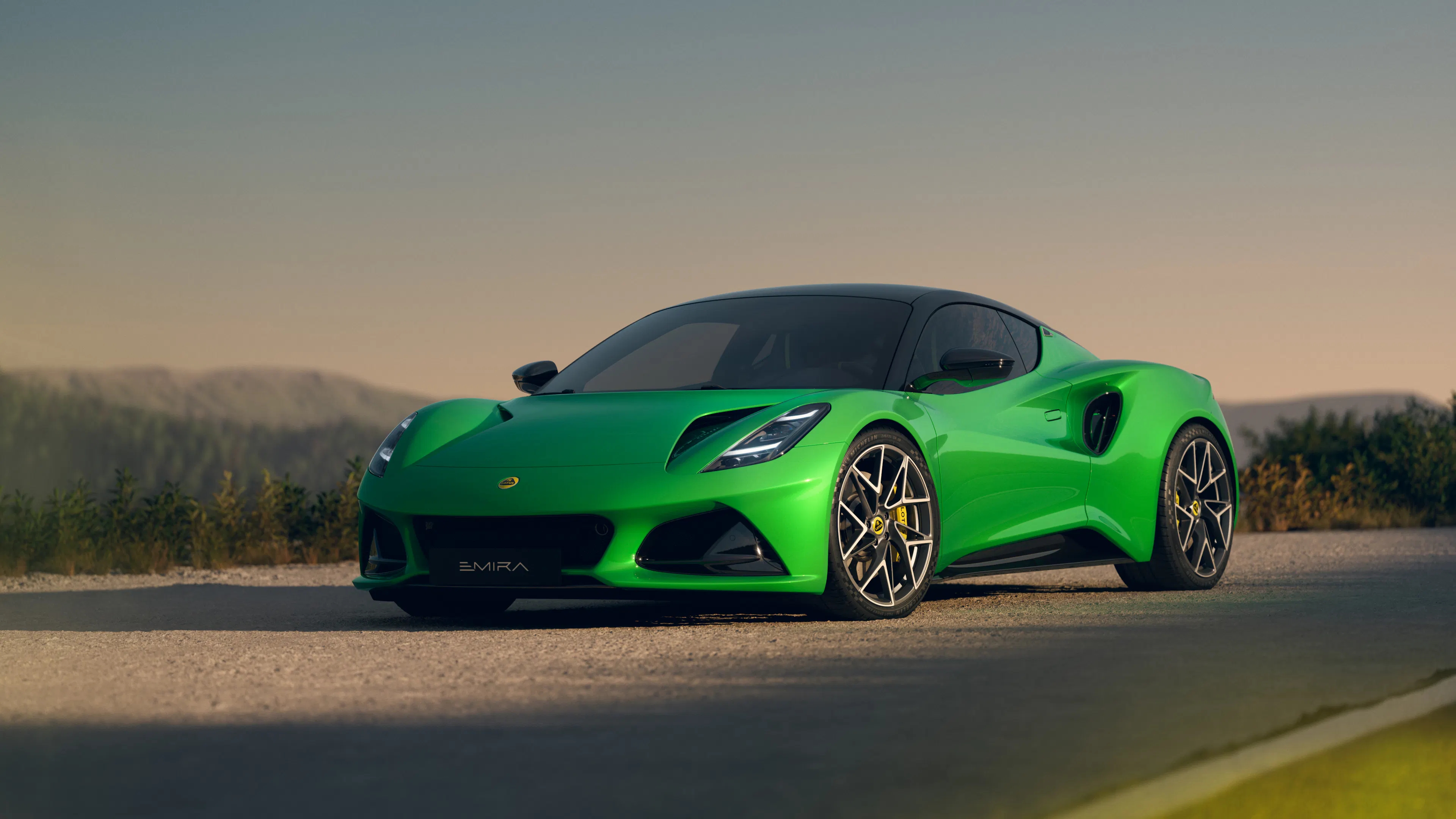 Lotus Emira V6 SE, statische Aufnahme von der Seite und Front auf einer Straße.