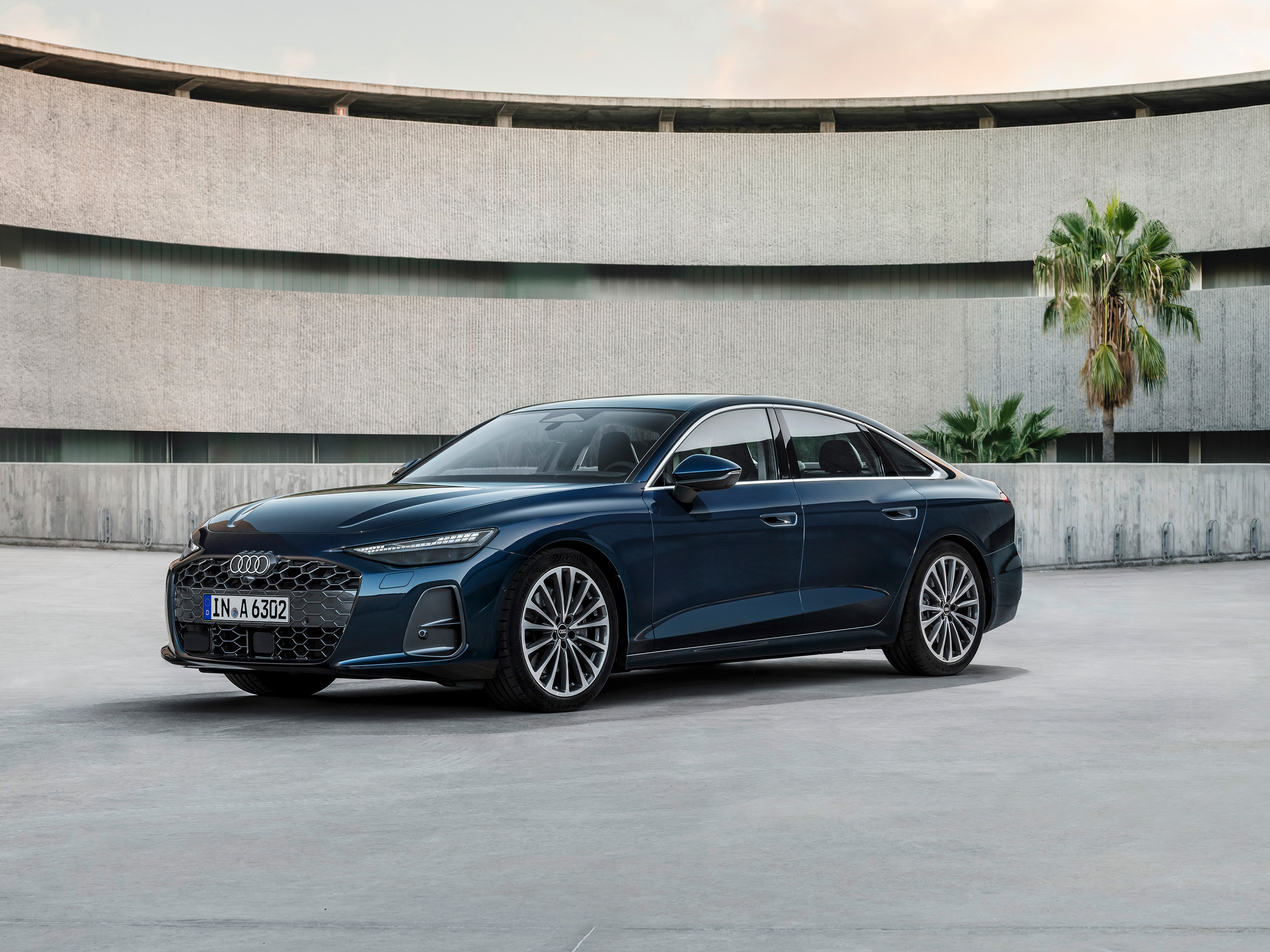 Dunkelblaue Audi-A6-C9-Limousine, schräg von vorn fotografiert vor einer Betonfassade mit Palme.