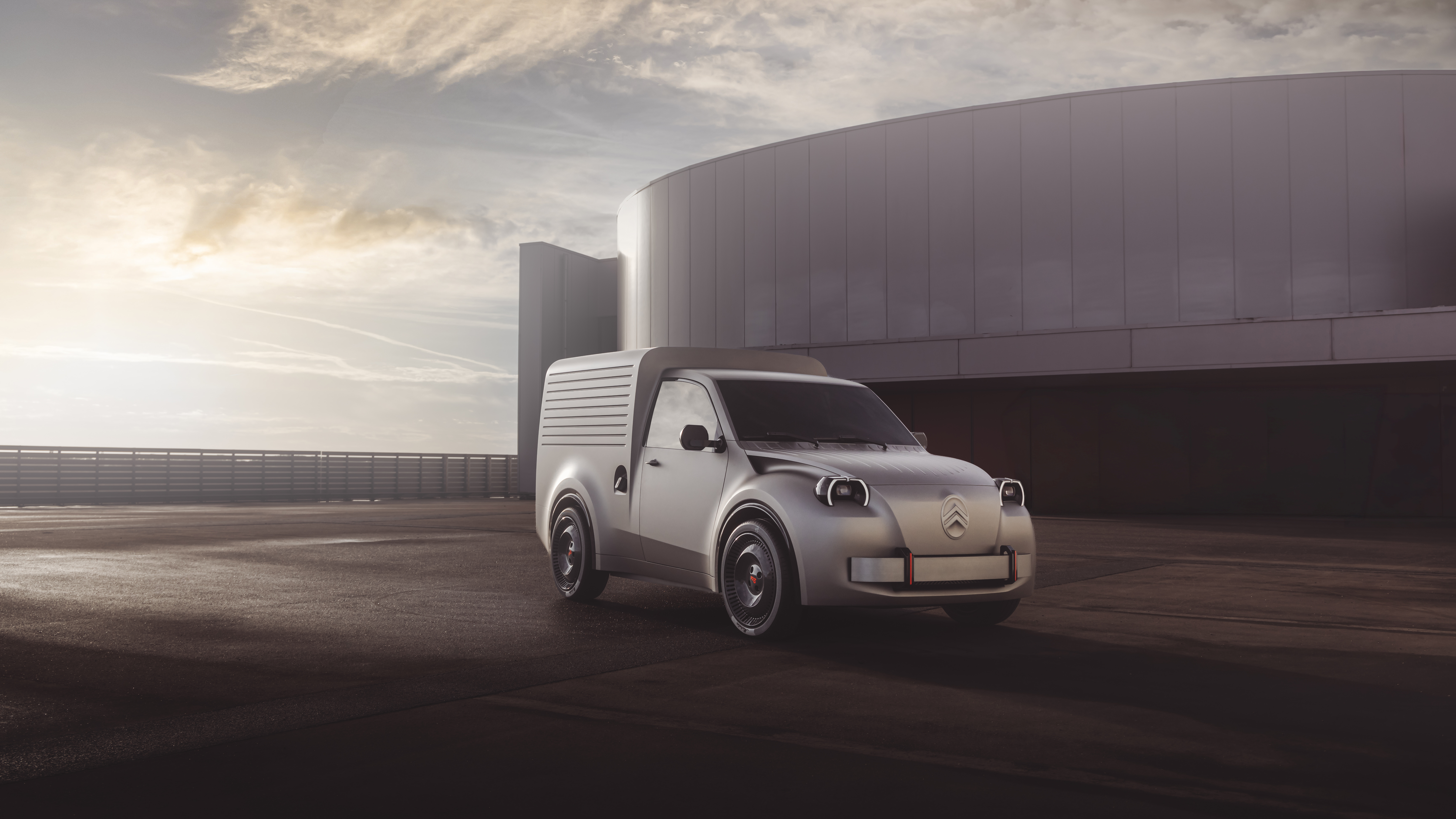 Graues Citroën 2CV Fourgonnette Concept mit hohem Kastenaufbau steht vor einem runden Gebäude im Abendlicht.