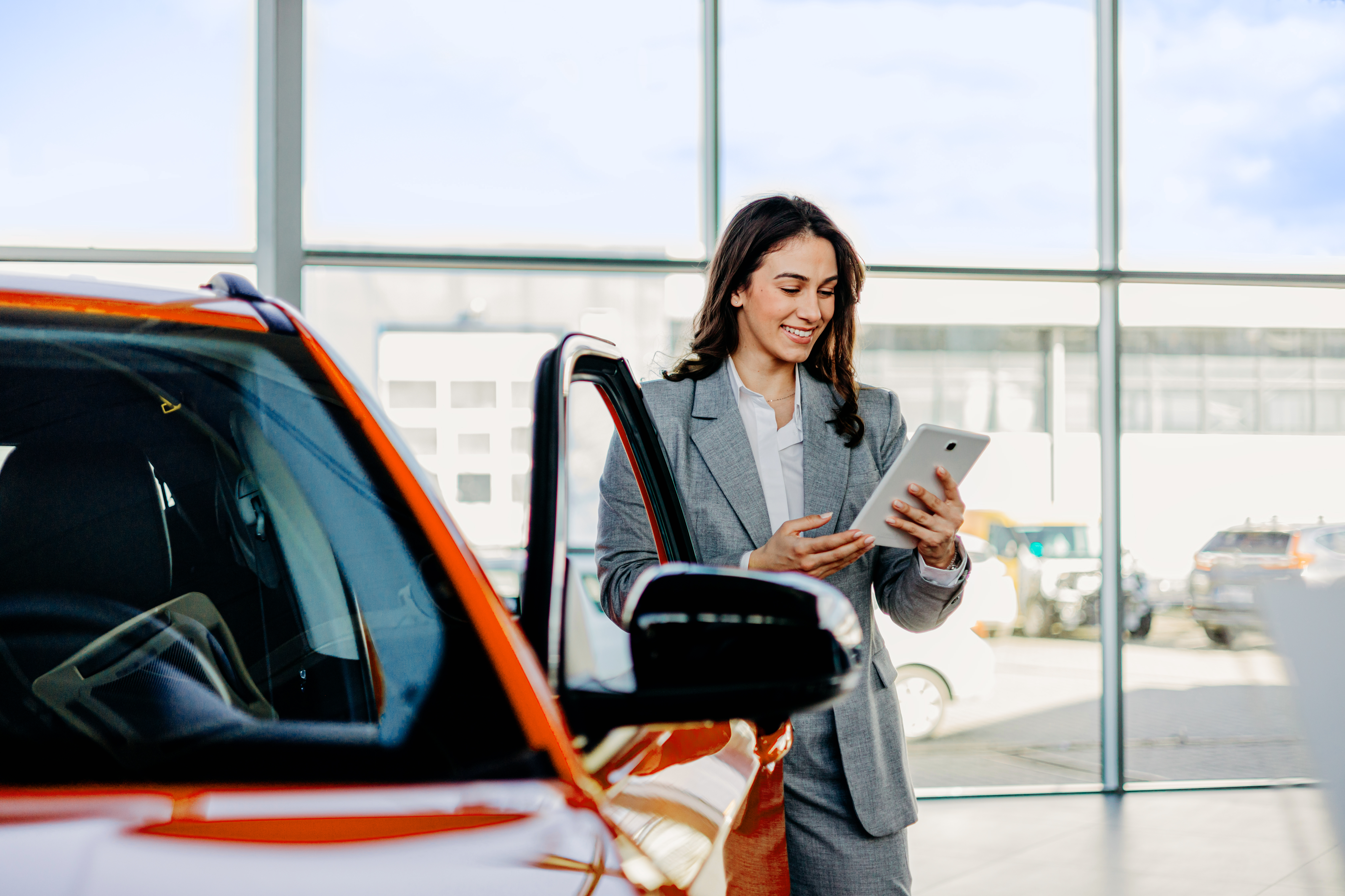 Eine Frau steht mit einem Tablet neben einem orangefarbenen Auto.