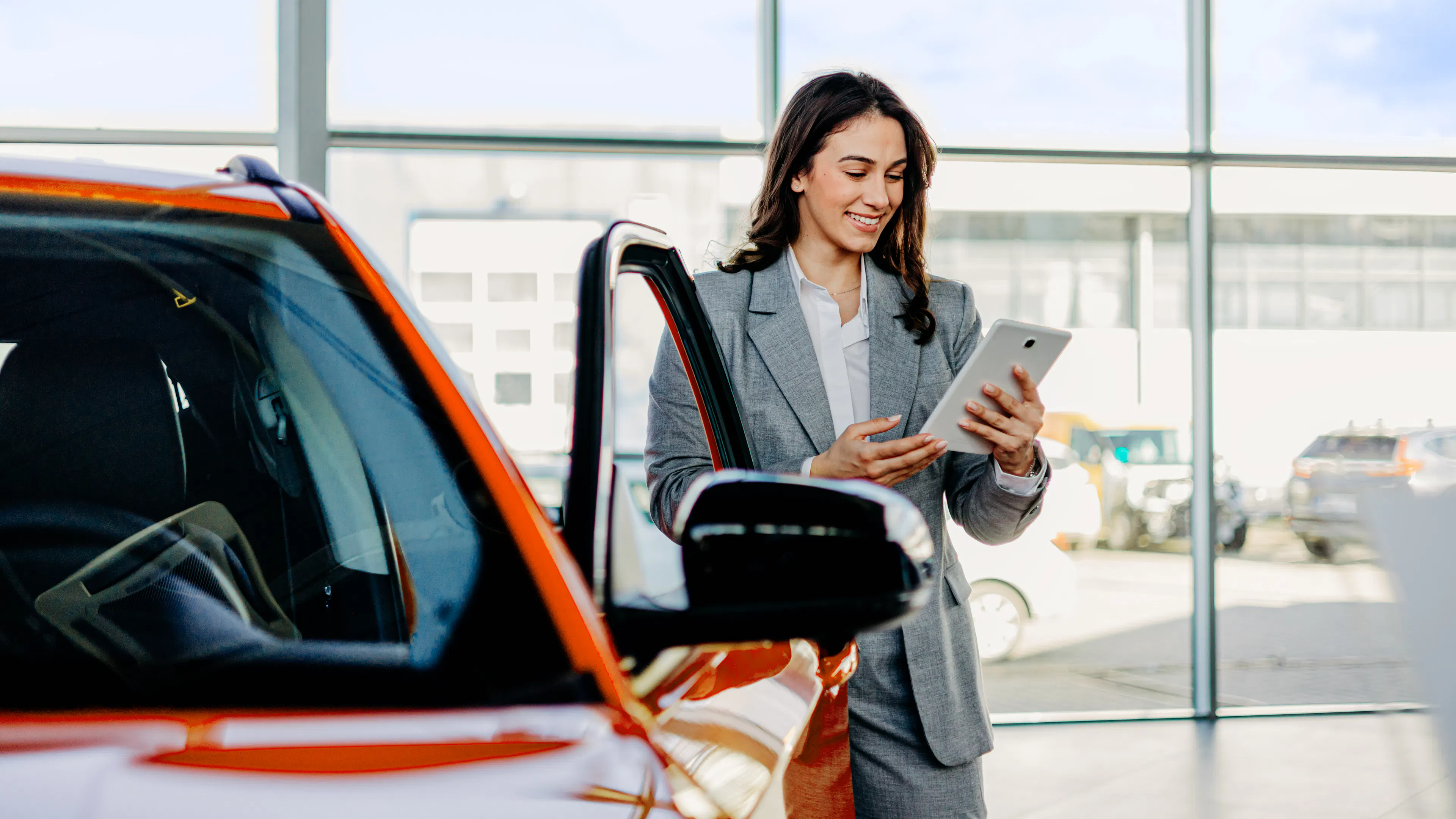 Eine Frau steht mit einem Tablet neben einem orangefarbenen Auto.