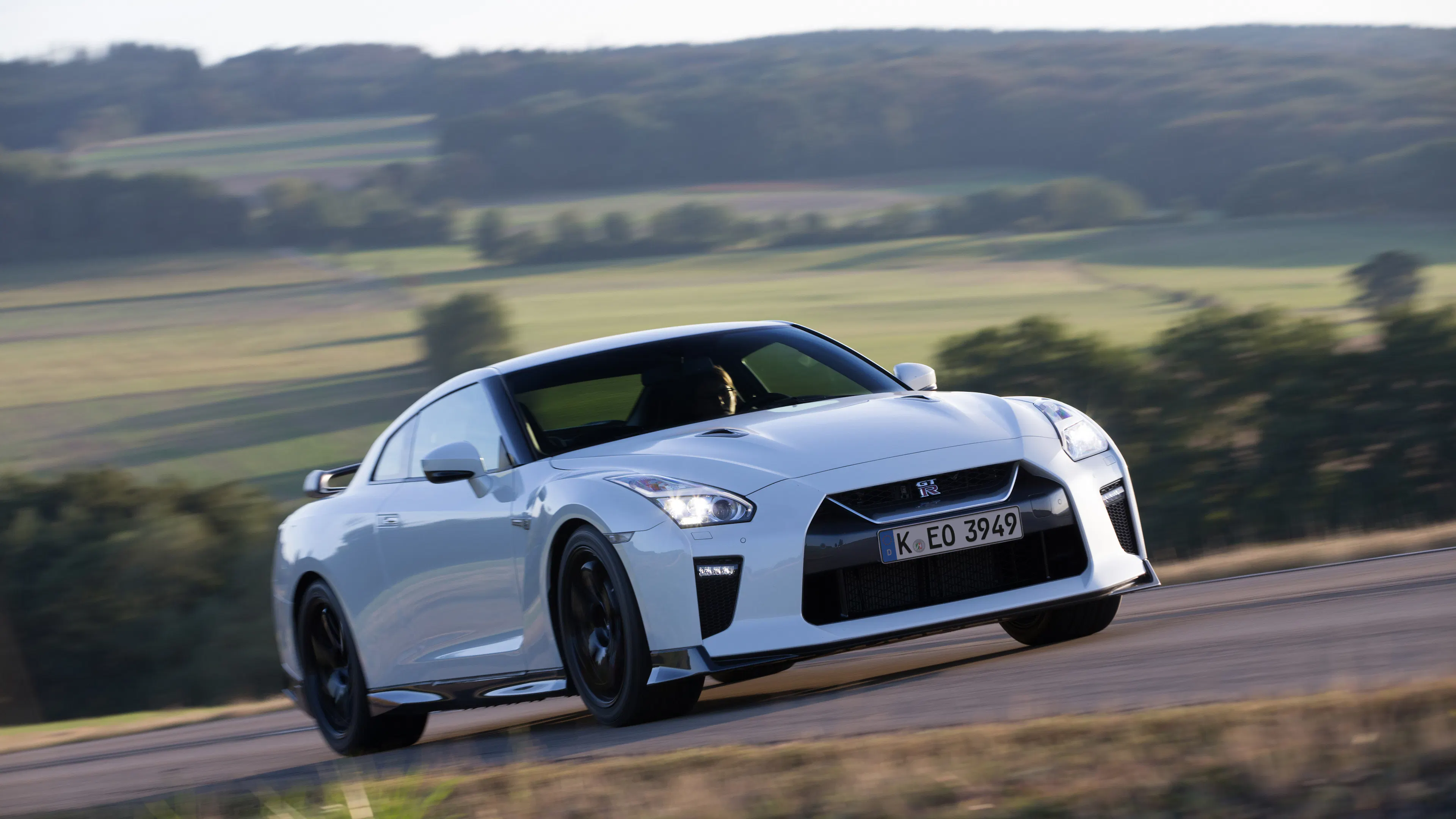 Ein weißer Nissan GT R fährt auf einer Landstraße.
