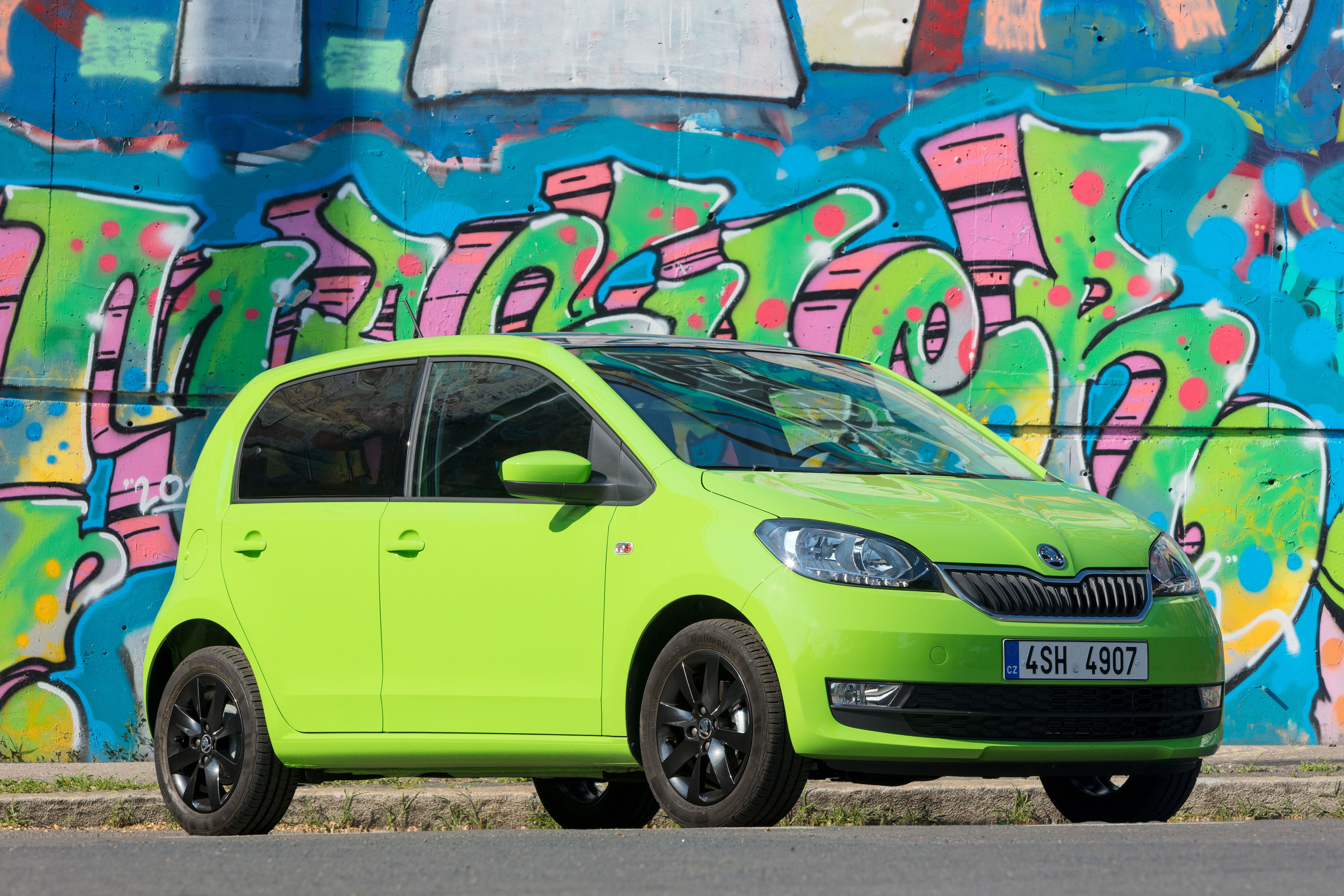 Hellgrüner Škoda Citigo mit schwarzen Felgen steht seitlich von vorn gesehen vor einer bunten Graffiti-Wand.