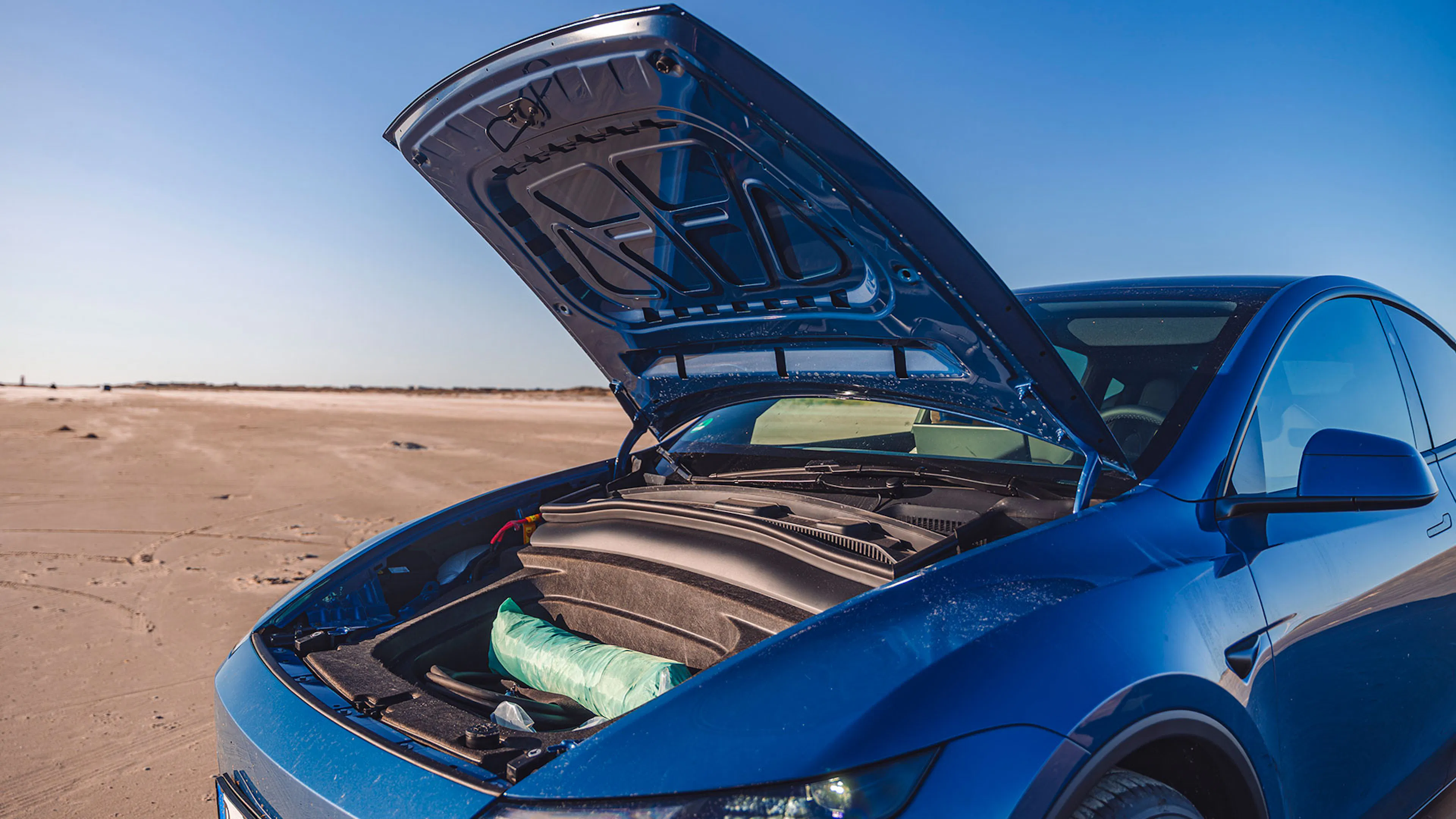 Die Frontklappe eines blauen Tesla Modell Y ist geöffnet und gibt den Blick auf den vorderen Kofferraum, den sogenannten Frunk frei.