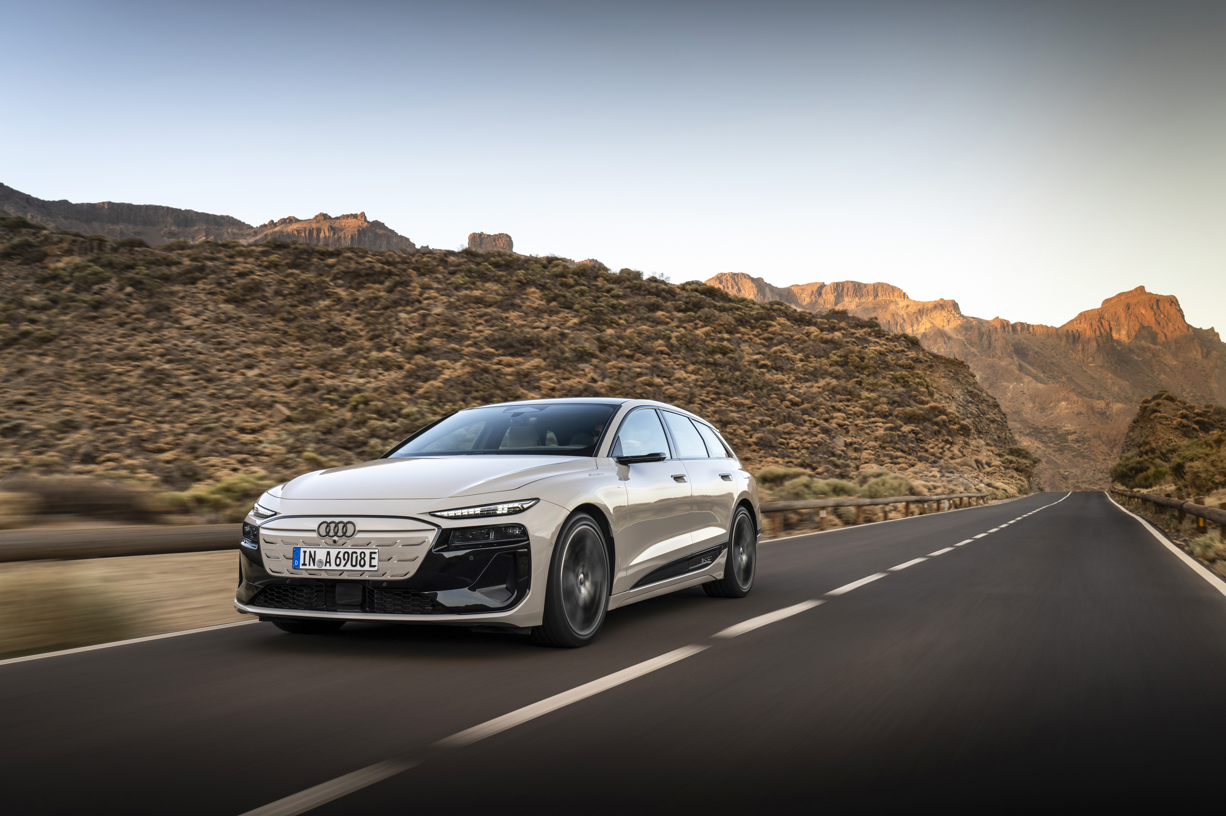 Cremefarbener Audi A6 e-tron in Fahrt auf einer Bergstraße vor felsiger Landschaft.