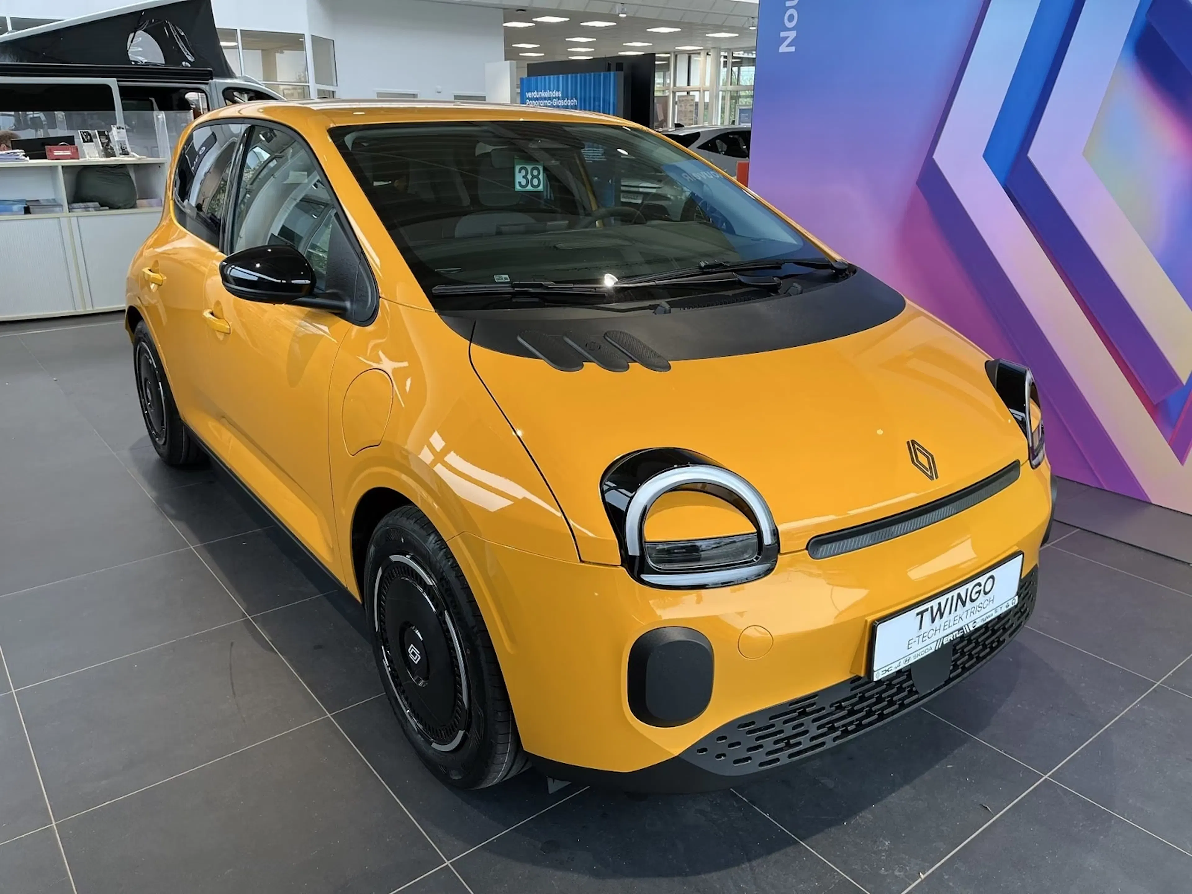 Mangogelber Renault Twingo E-Tech in einem Verkaufsraum.