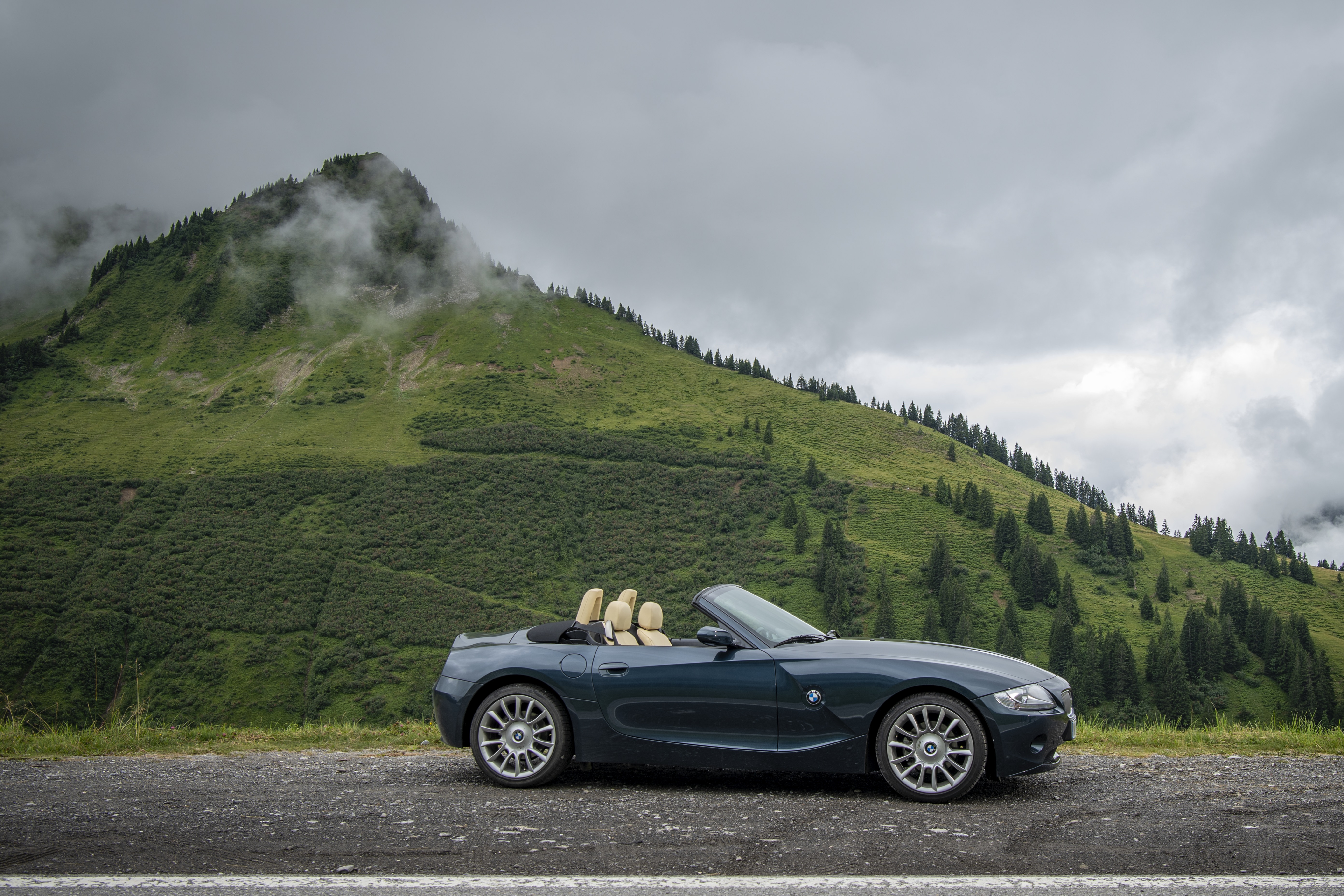 Dunkelgrüner BMW Z4 E85 Roadster steht seitlich geparkt vor einem bewaldeten Berg.