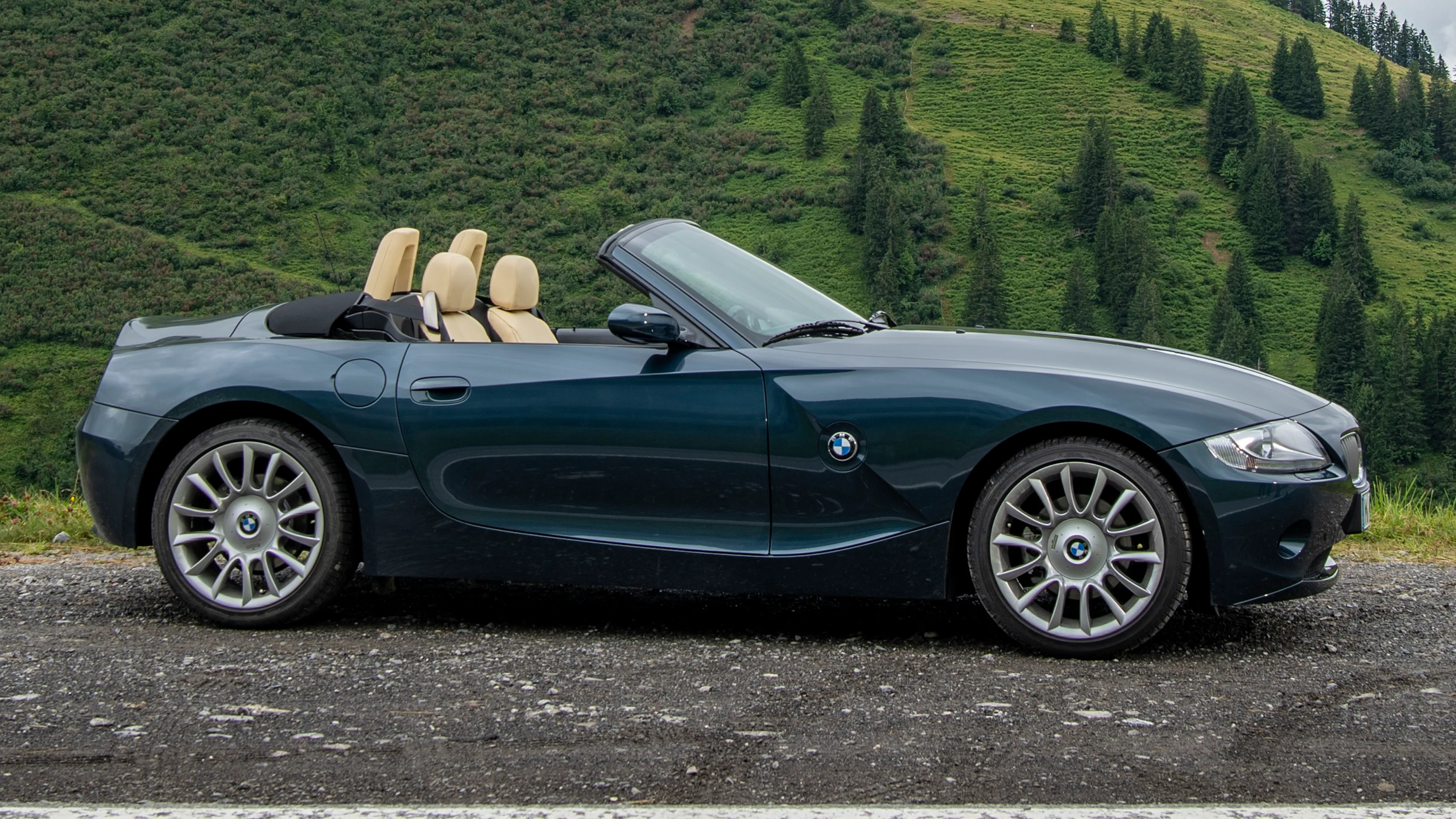 Dunkelgrüner BMW Z4 E85 Roadster steht seitlich geparkt vor einem bewaldeten Berg.