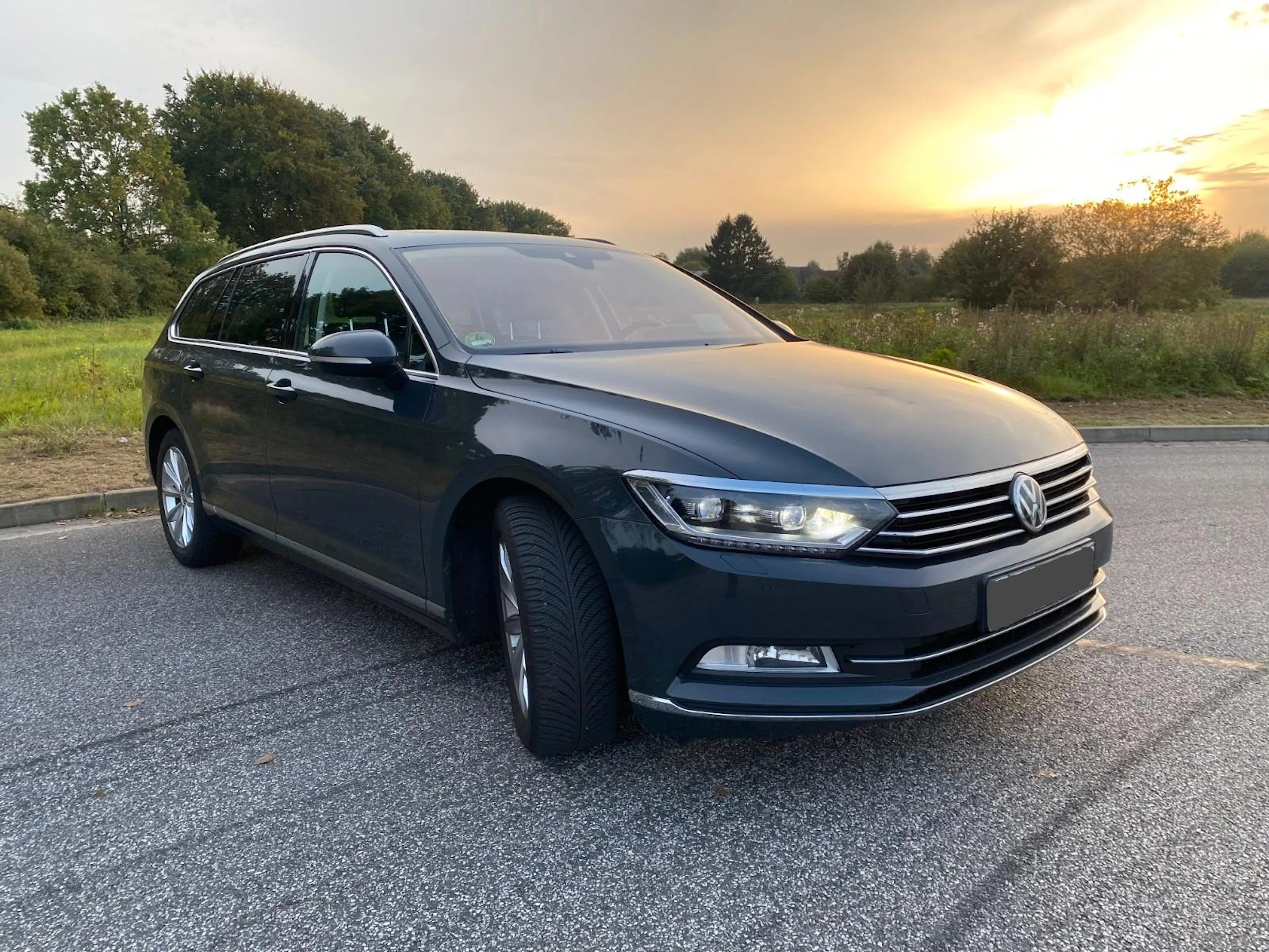 Ein grauer VW Passat steht auf einer befestigten Fläche im Sonnenuntergang.