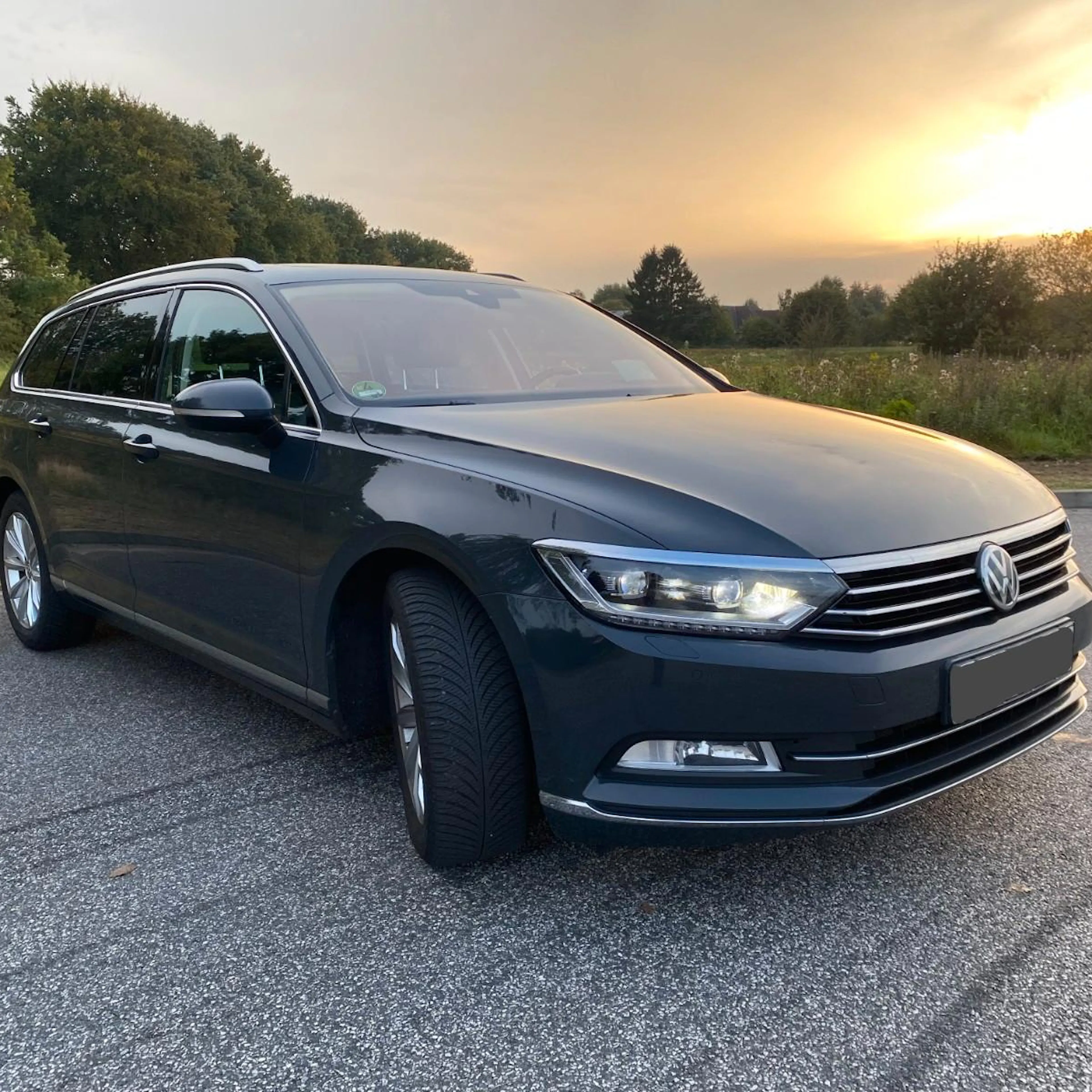 Ein grauer VW Passat steht auf einer befestigten Fläche im Sonnenuntergang.