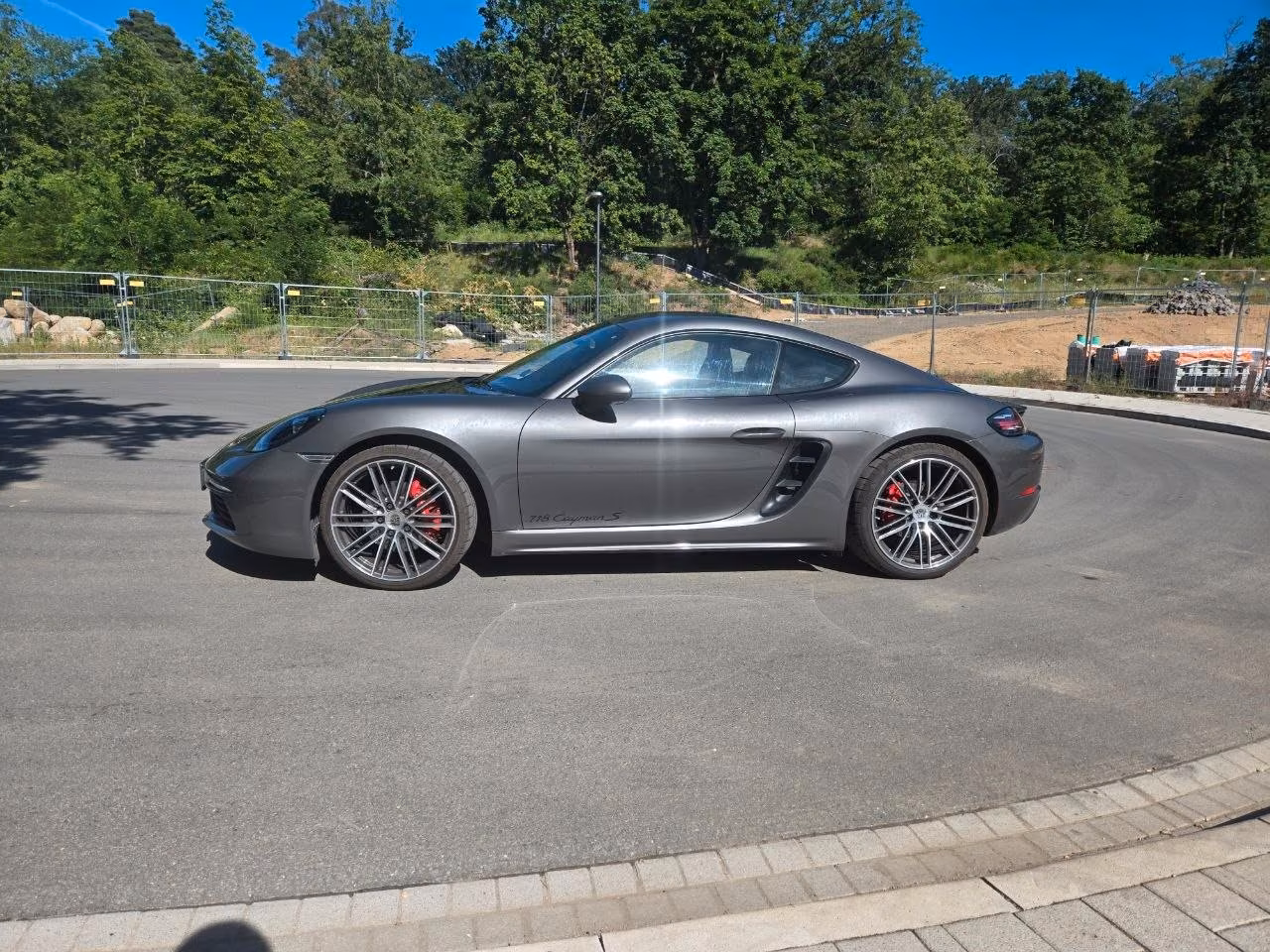 Ein grauer Porsche Cayman steht auf einer gepflasterten Fläche.