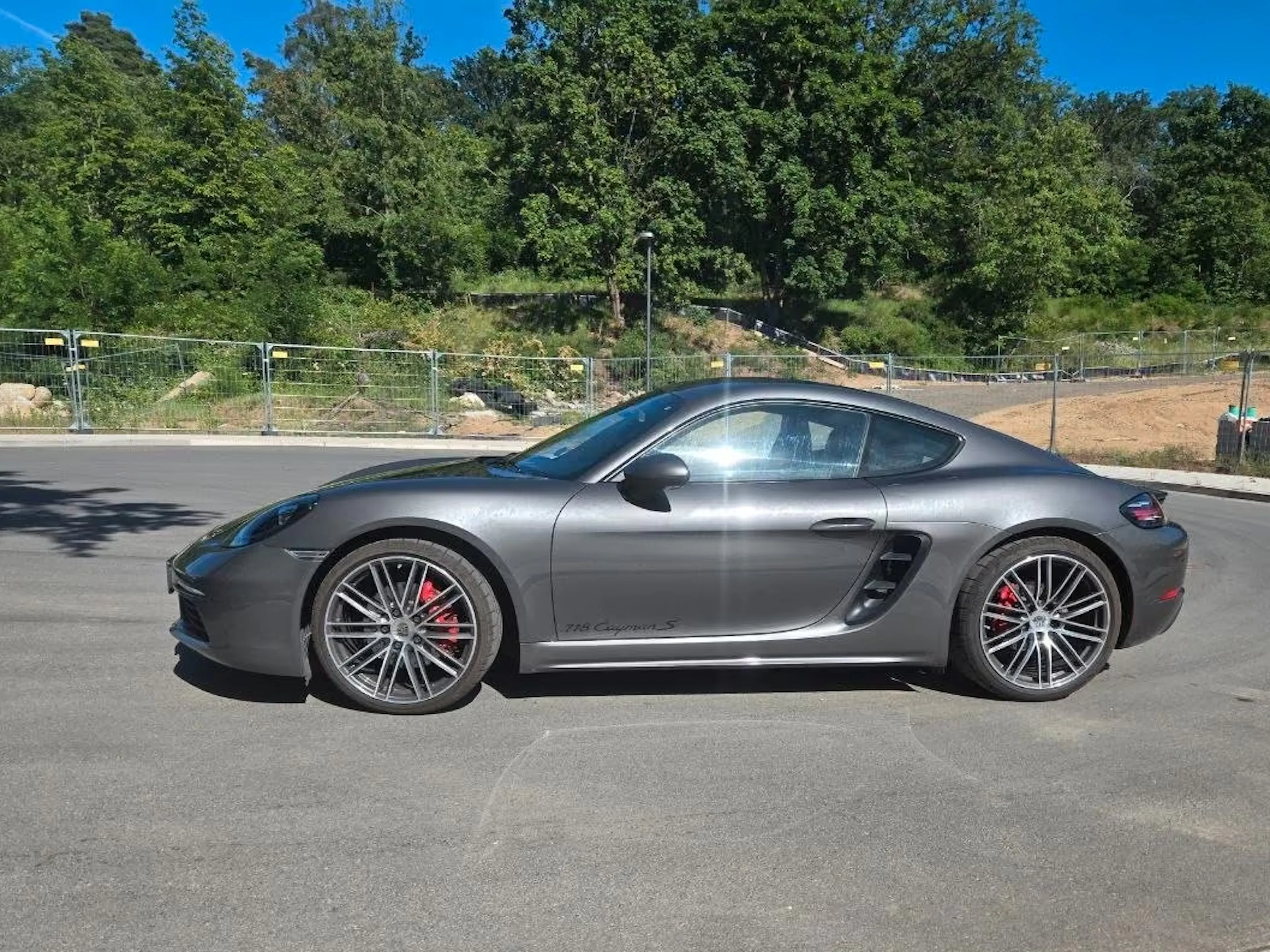Ein grauer Porsche Cayman steht auf einer gepflasterten Fläche.