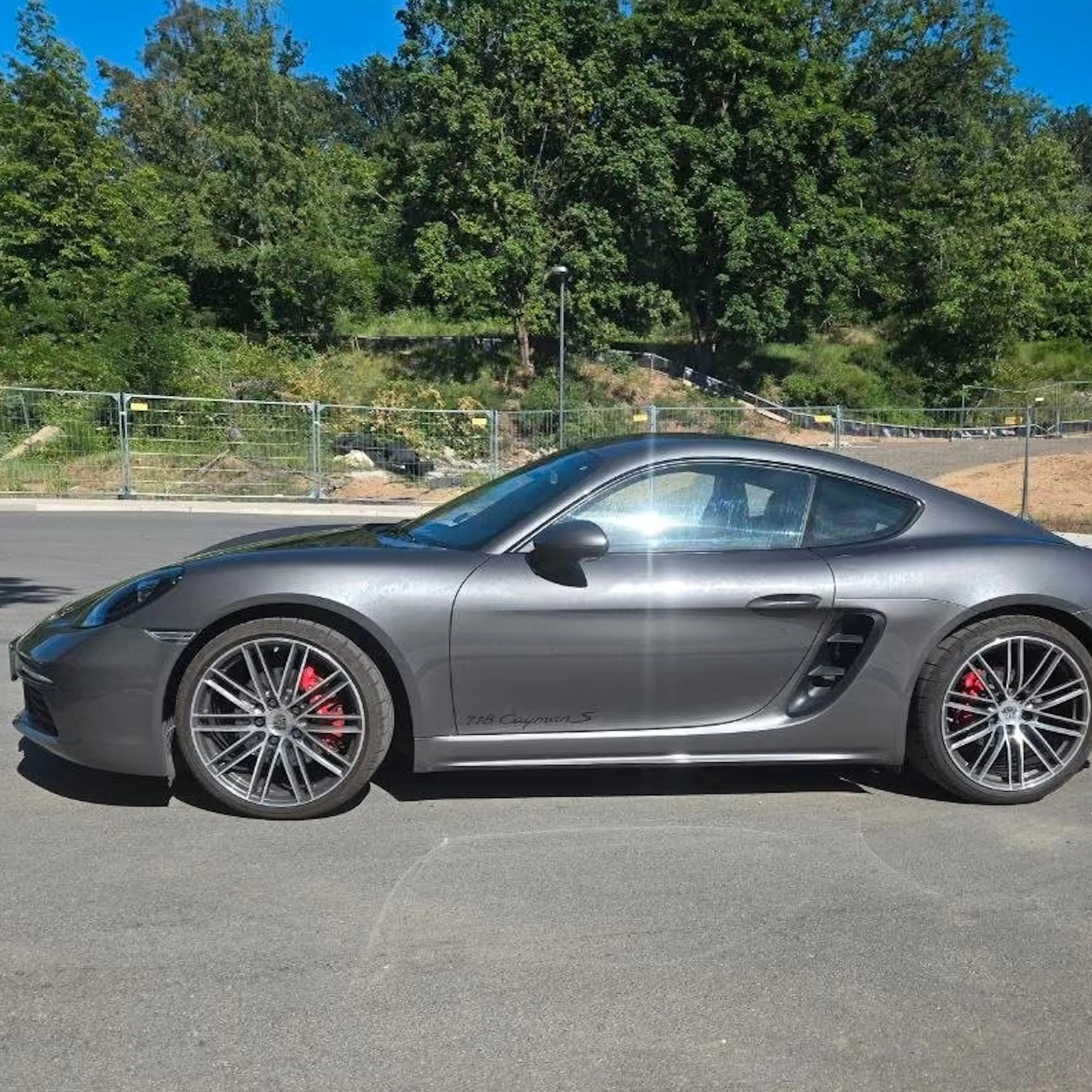 Ein grauer Porsche Cayman steht auf einer gepflasterten Fläche.