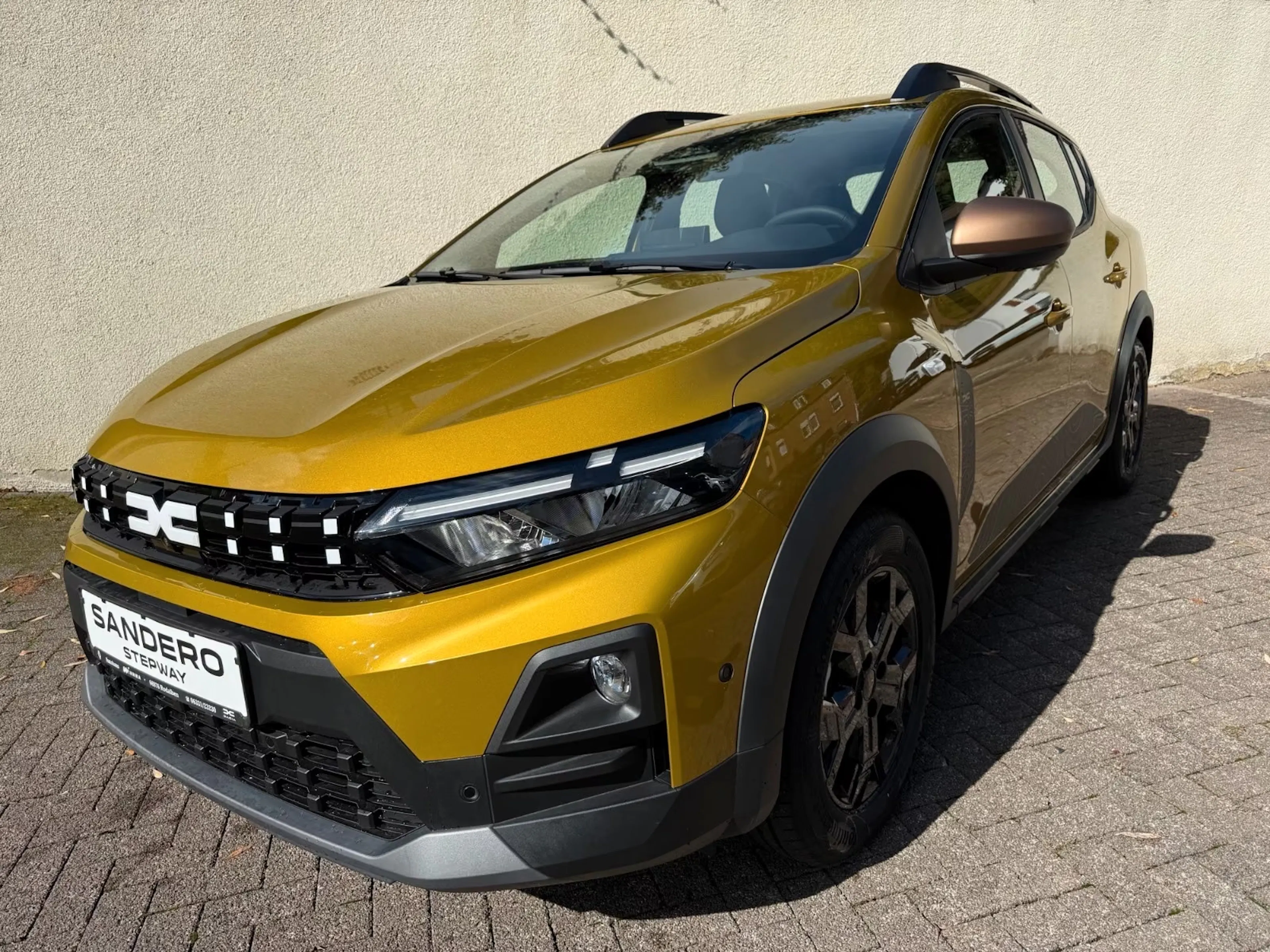 Ein goldgelber Dacia Sandero Stepway Hybrid steht auf einer gepflasterten Fläche.